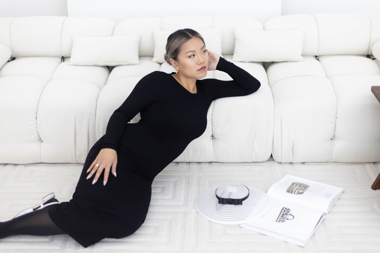 Woman wearing a black dress lounges on white sofa with notebook and pen nearby.