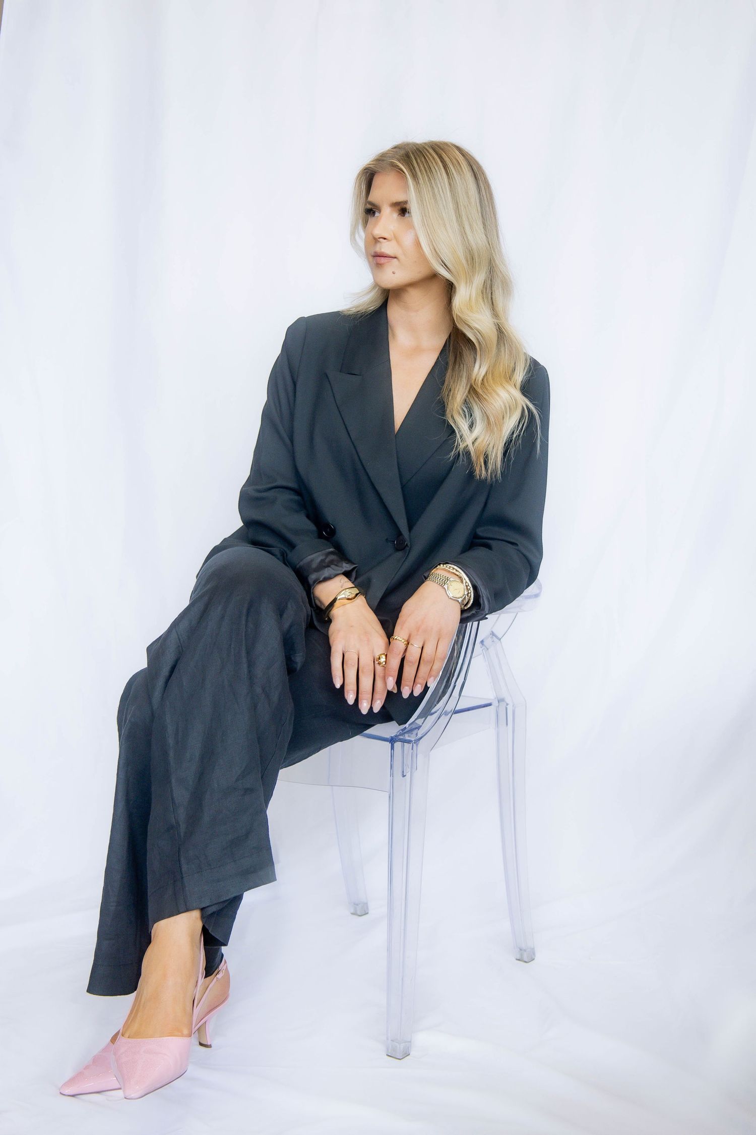 Professional fashion photo of black blazer outfit with pink shoes on clear chair against white backdrop.