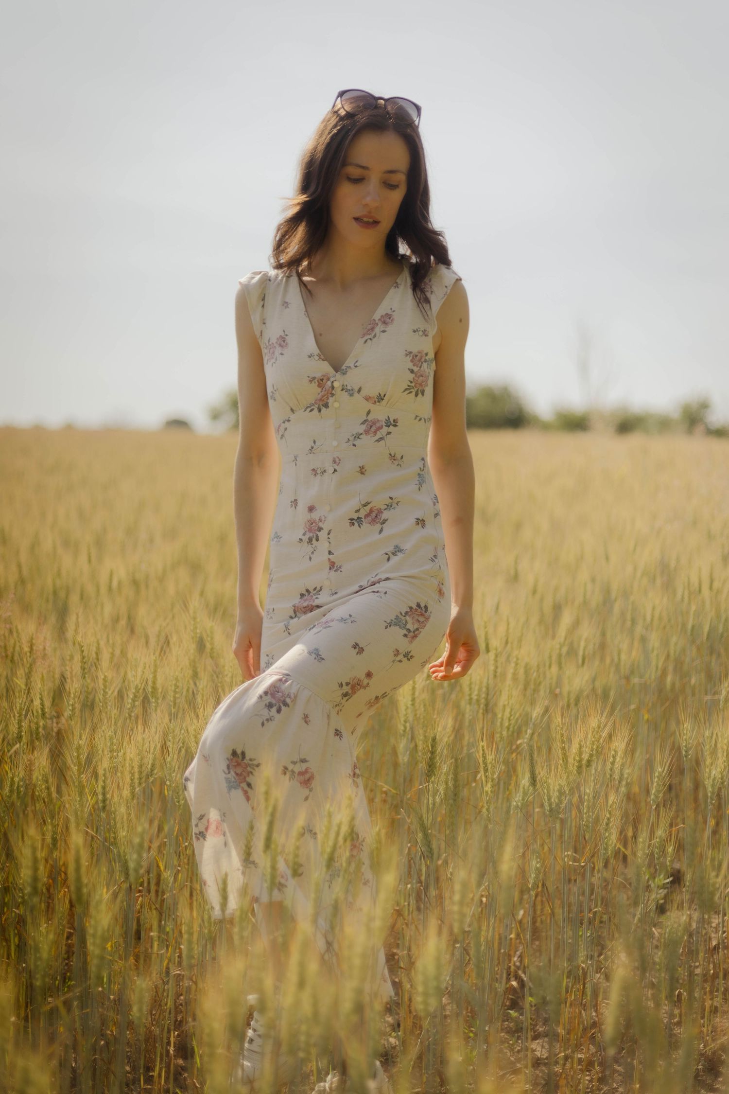 Woman in floral dress walks through golden wheat field during sunset photoshoot.