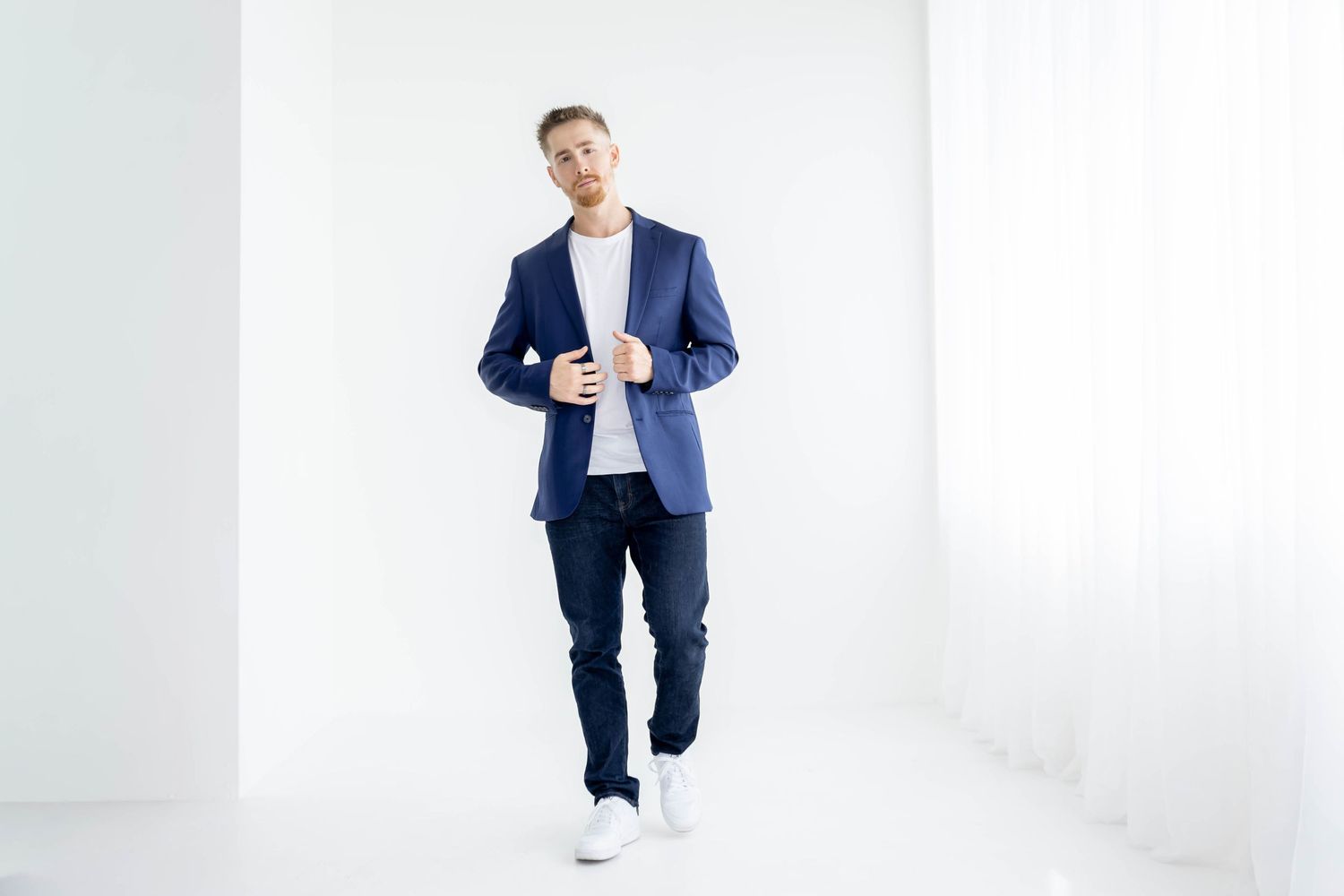 Person in navy blazer and jeans standing against white wall in bright modern space.