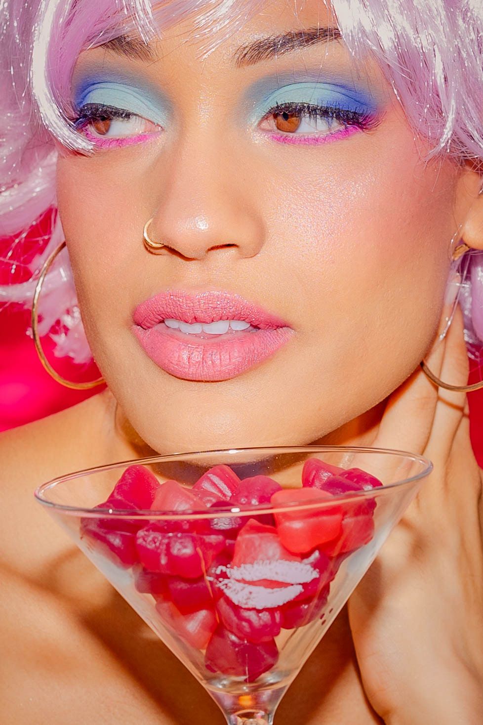 Artistic beauty portrait with pink tones and martini glass filled with rose petals.