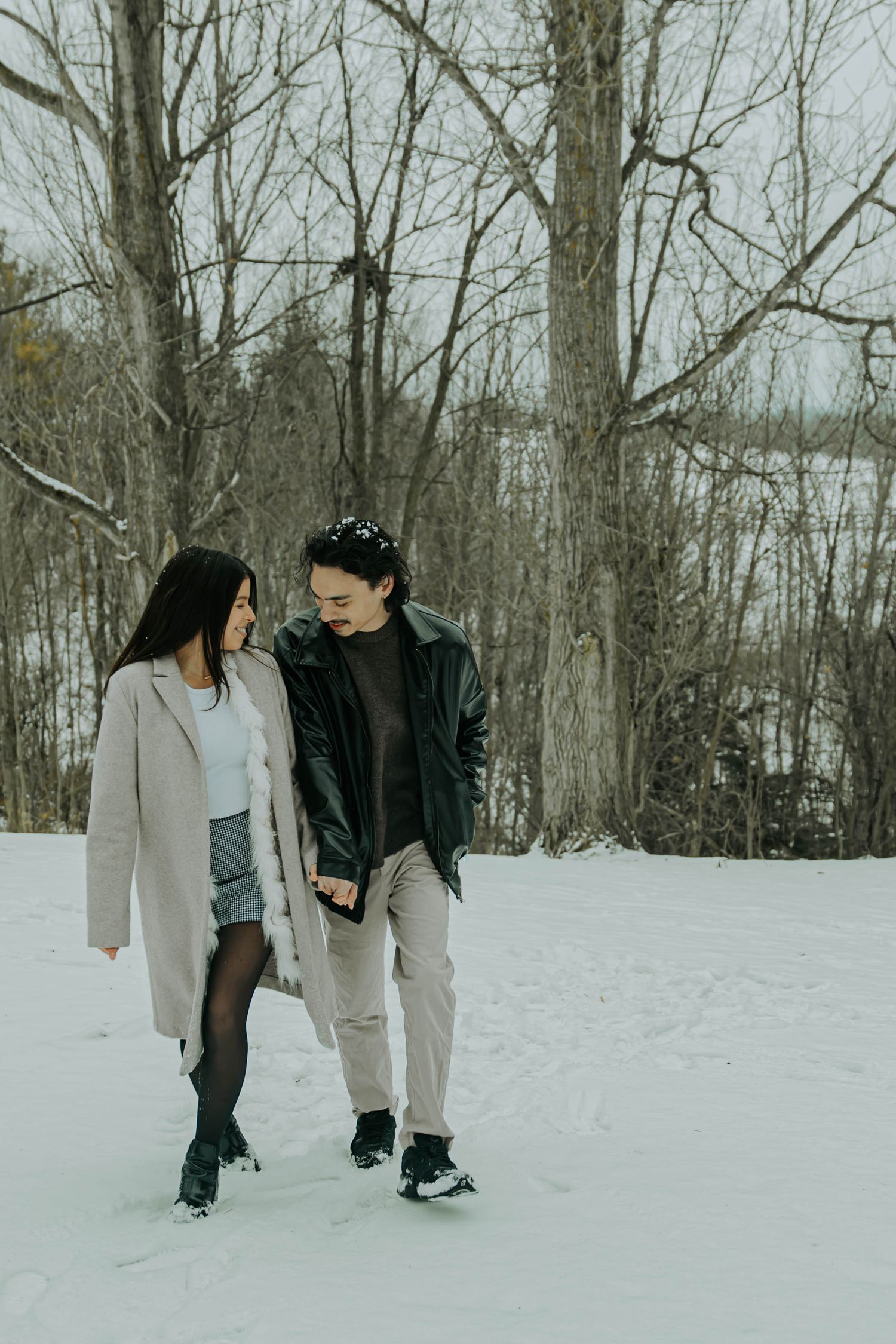 A couple walks together through a snowy winter forest landscape in matching casual outfits.