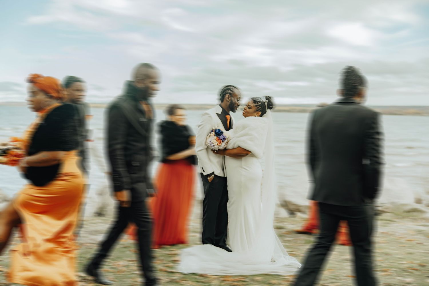 Blurred motion shot of wedding party walking along beach in orange and black attire.