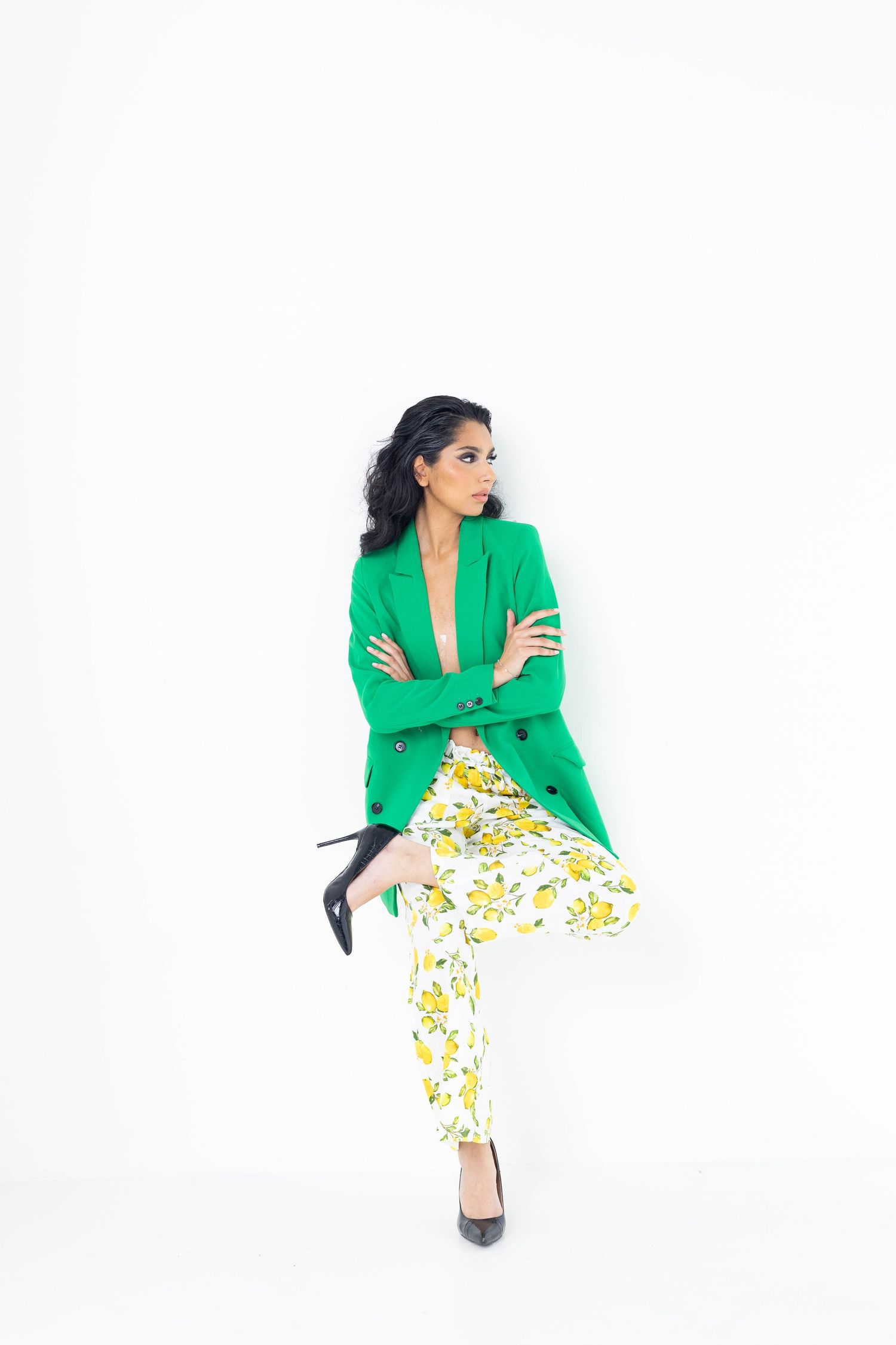 A woman wearing a vibrant green blazer and floral print pants poses against a white background with black heels.