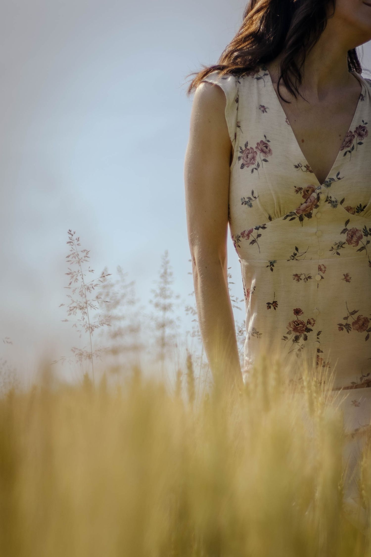 Artistic shot of floral dress detail with wheat field and trees in soft focus.