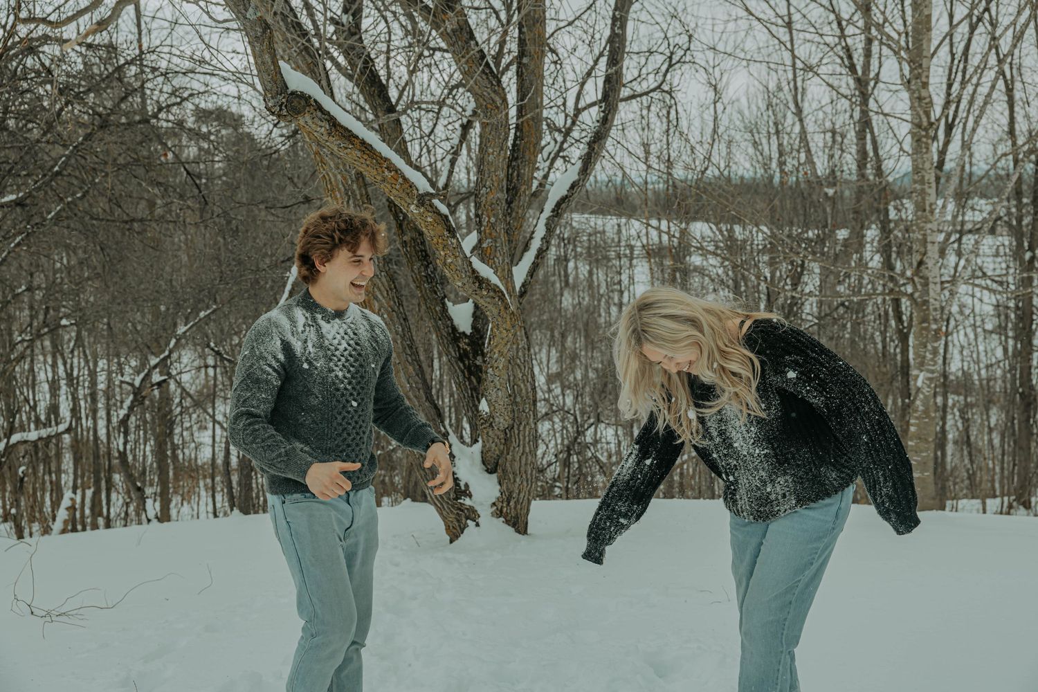 A group of winter sports enthusiasts skate in formation on a snowy outdoor ice rink surrounded by bare trees.
