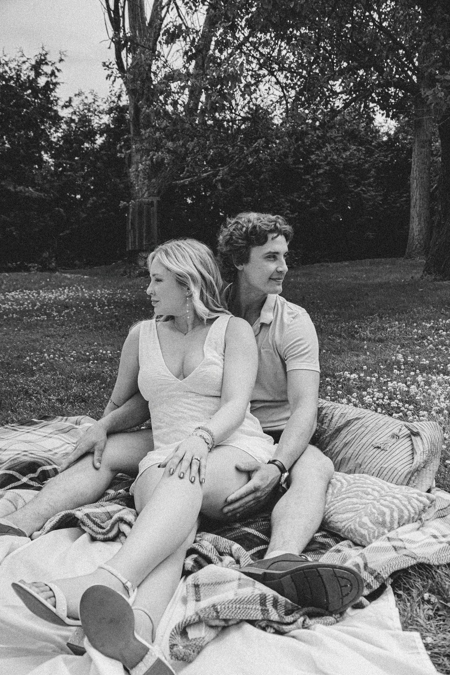 Black and white photo of a couple relaxing on blankets in a grassy field.