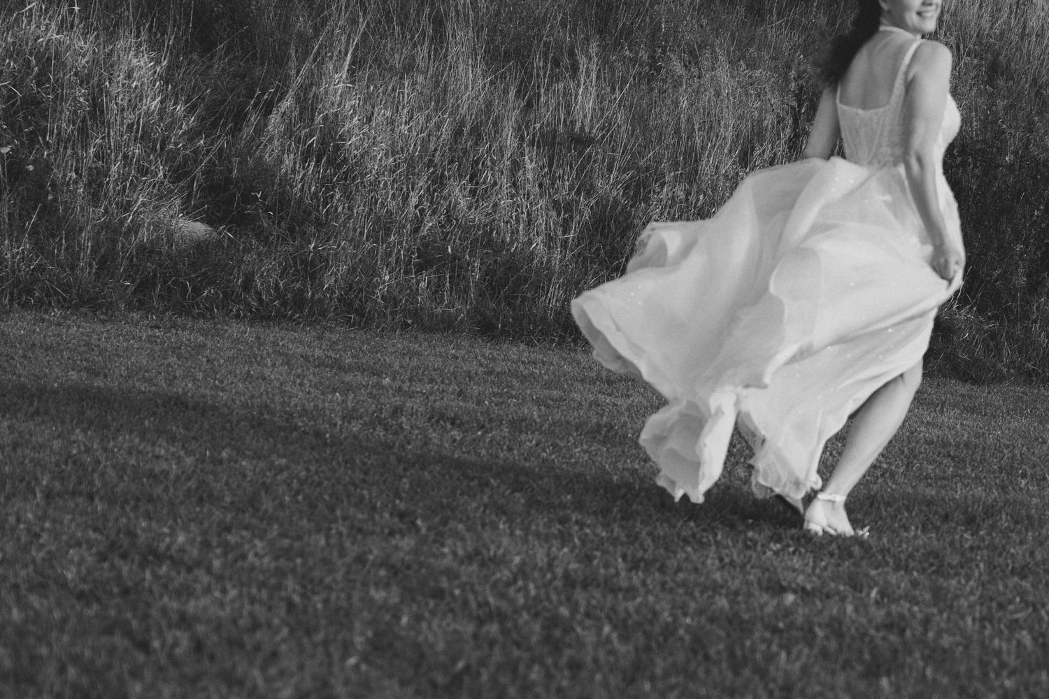 A person in a flowing white dress twirls gracefully in a grassy field at sunset.
