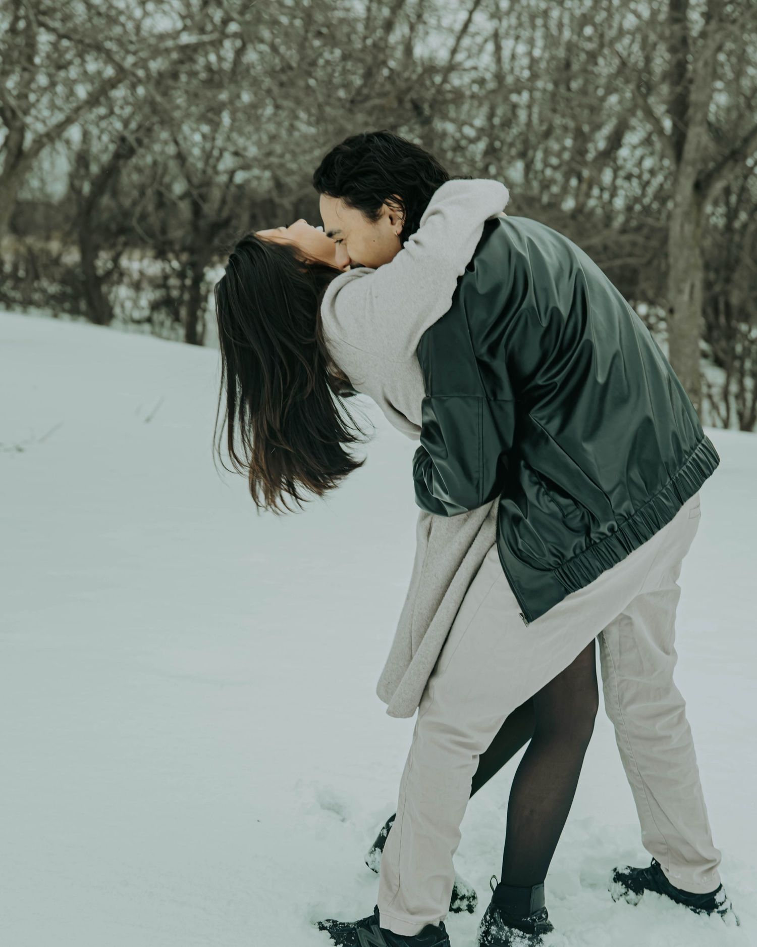 A couple plays together in the snow, bending down to gather snow in a winter landscape.