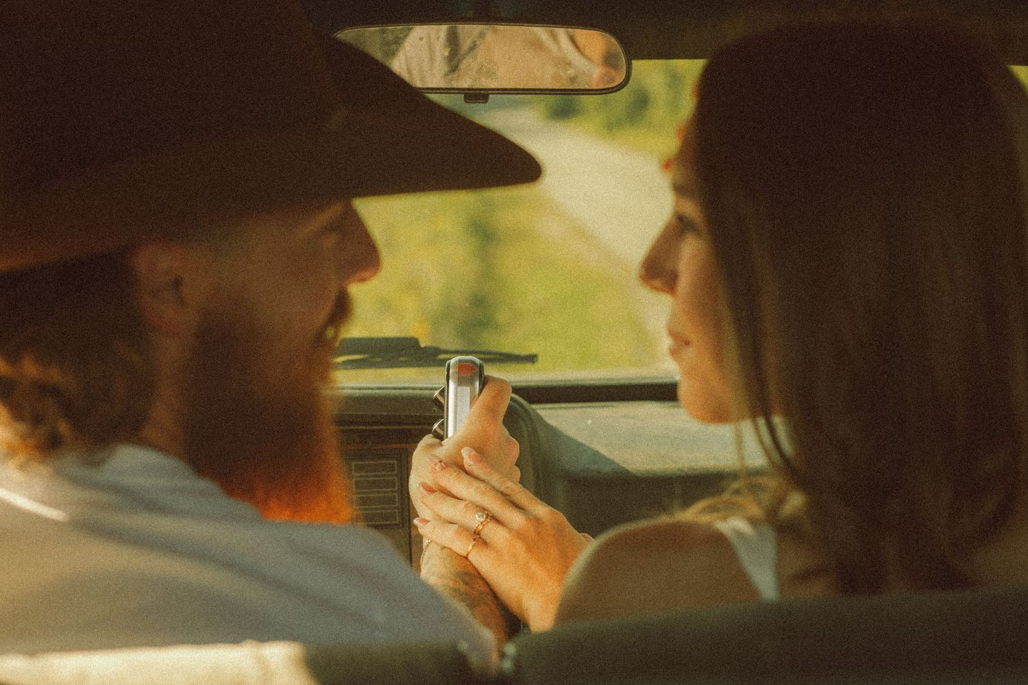 Couple sharing a romantic moment inside a vintage car, man in cowboy hat holding a phone.