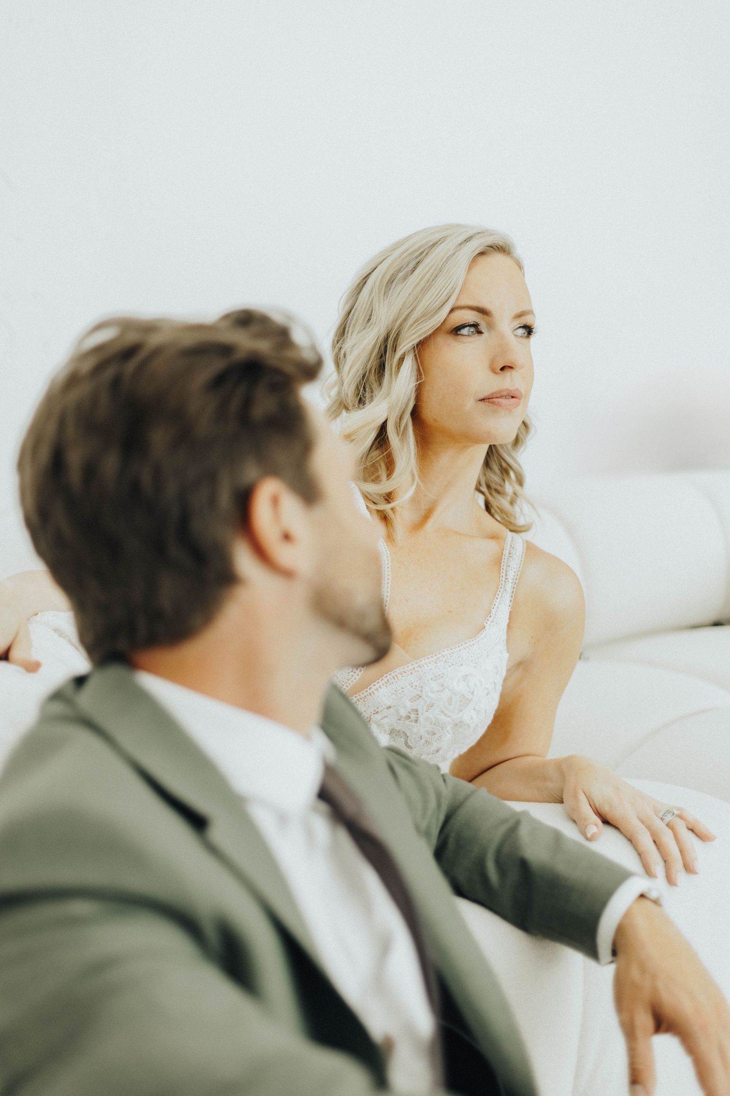 Beautiful bride in white lace dress sits with groom in olive suit during intimate wedding moment.