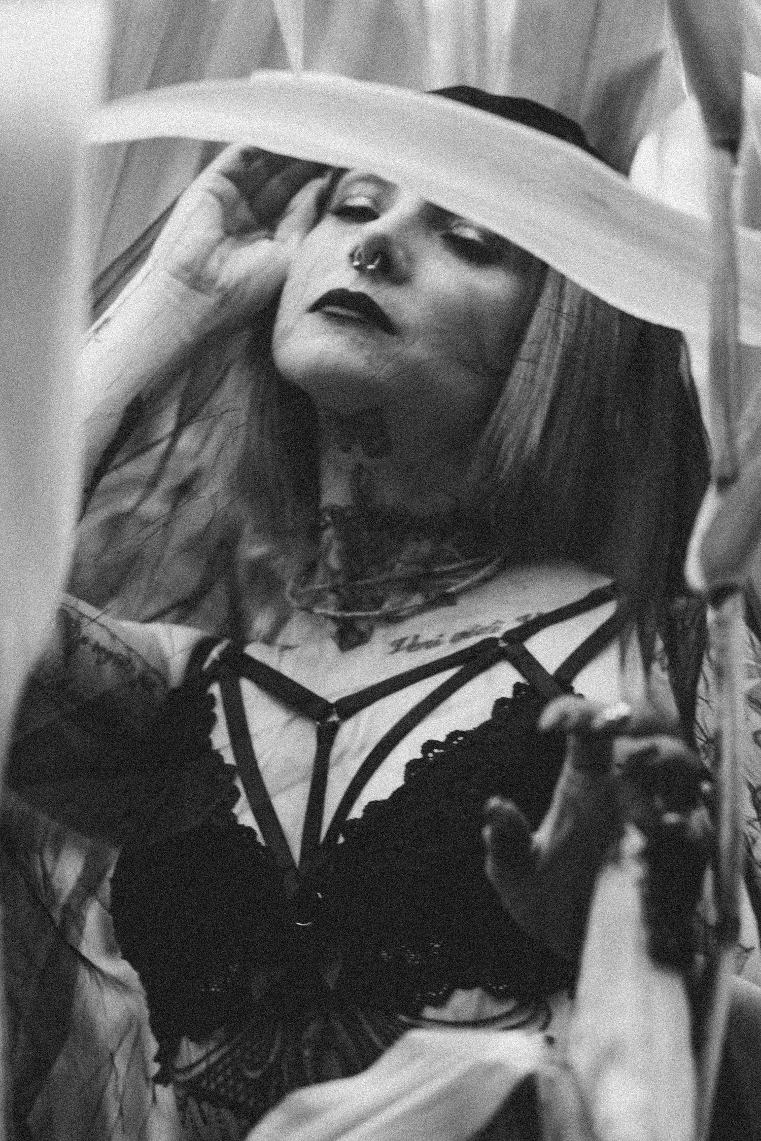 Black and white photo of a tattooed woman with nose ring wearing lace lingerie and sheer robe in gothic style.