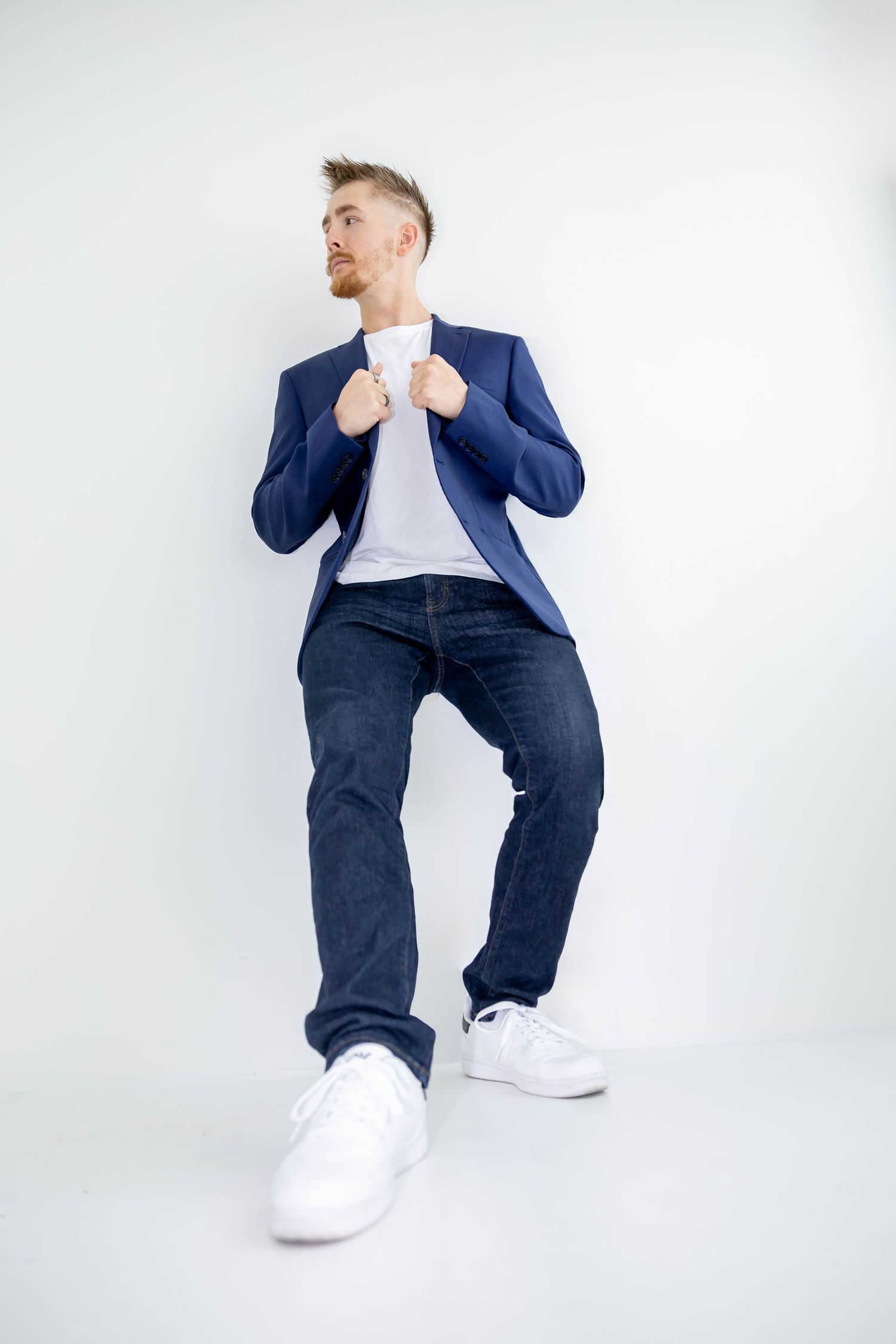 Figure in navy blazer and jeans strikes dynamic poses against white background wearing white sneakers.
