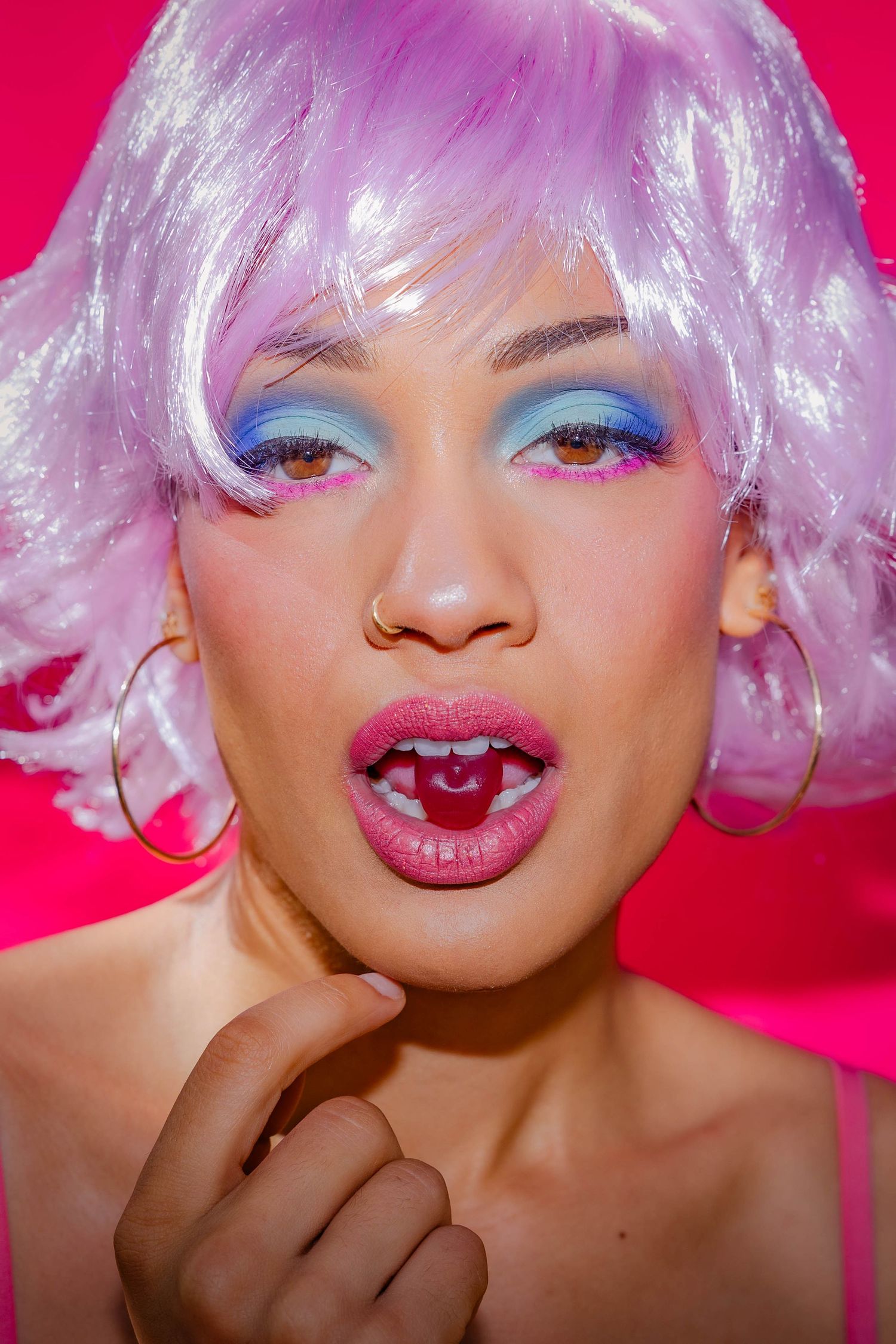 Whimsical beauty shot featuring pink hair and vibrant makeup against hot pink background.