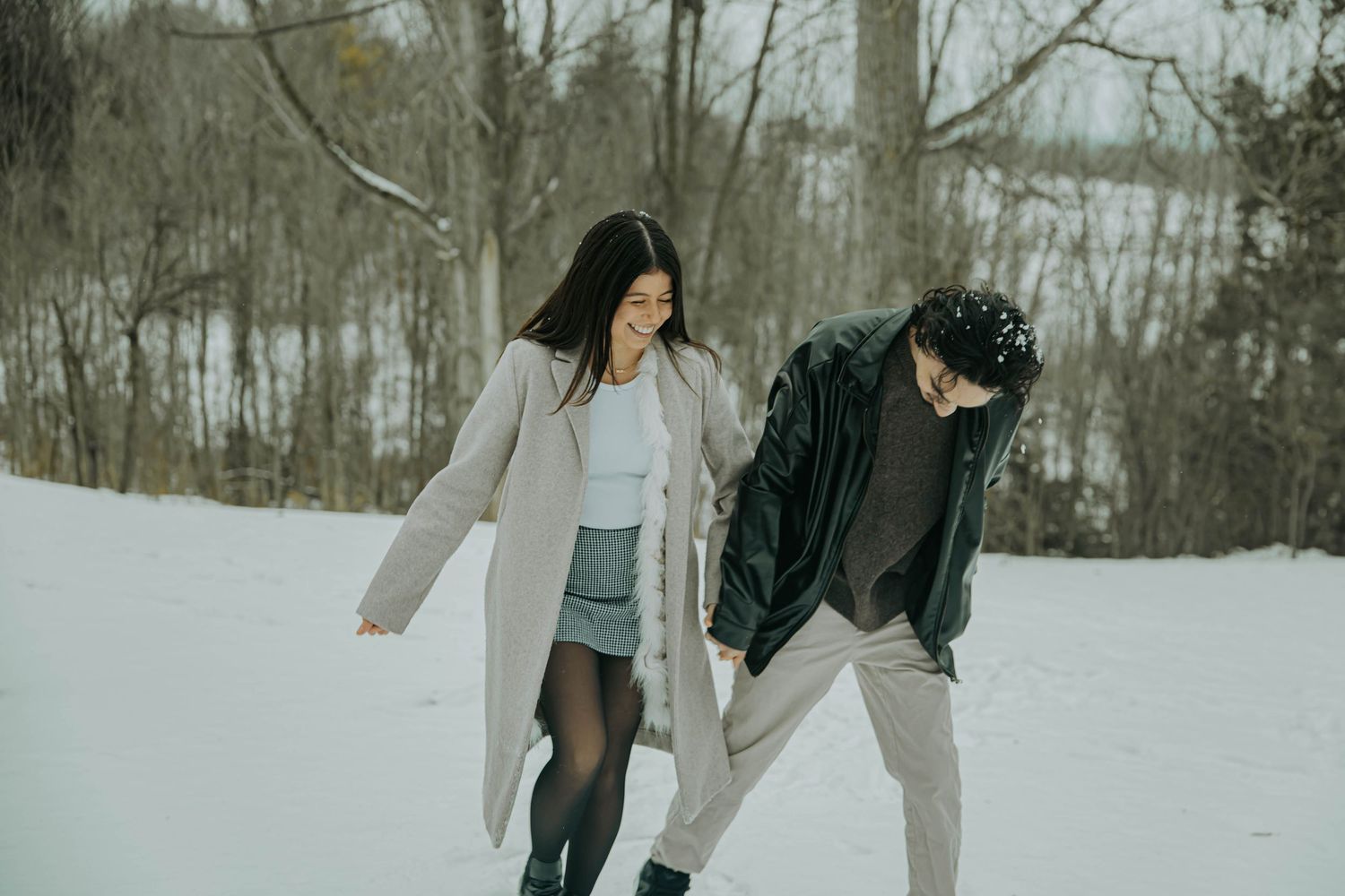 Two people walk together through a snowy winter landscape wearing cozy coats and holding hands.