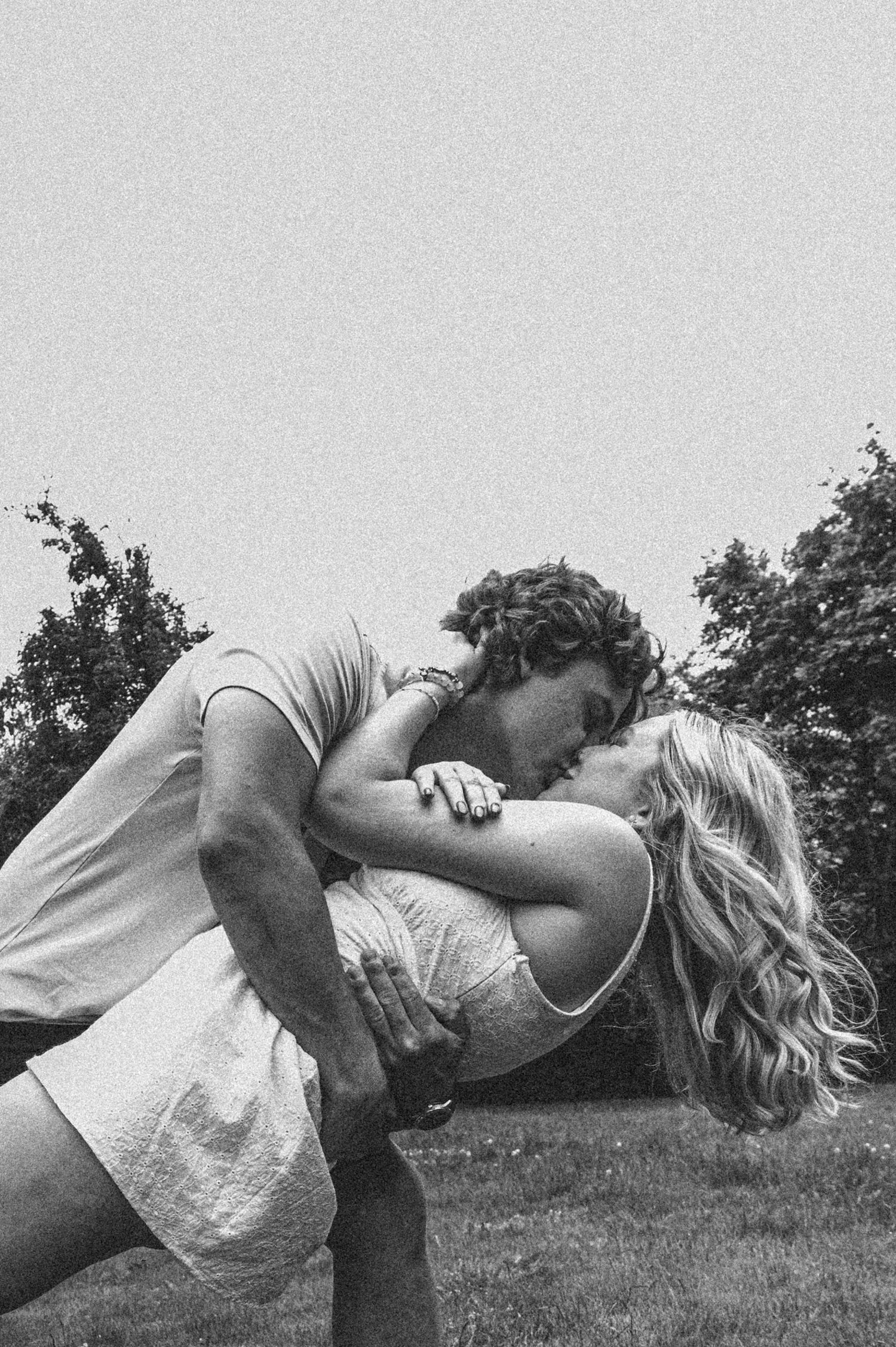 Black and white romantic photo sequence showing a couple embracing and dipping in a grassy field.