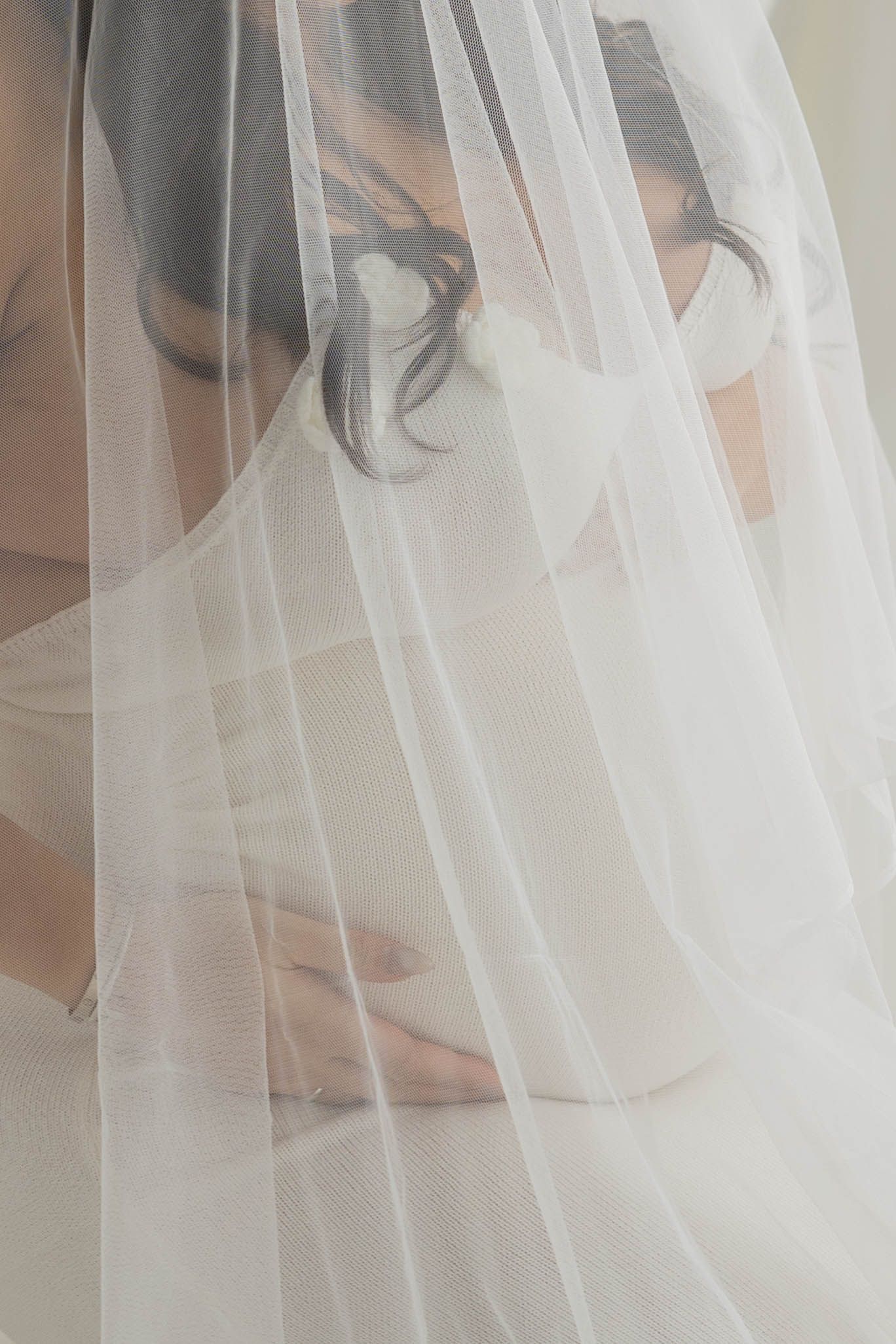 A delicate white wedding veil flows softly in front of a light-colored background creating an ethereal bridal detail.