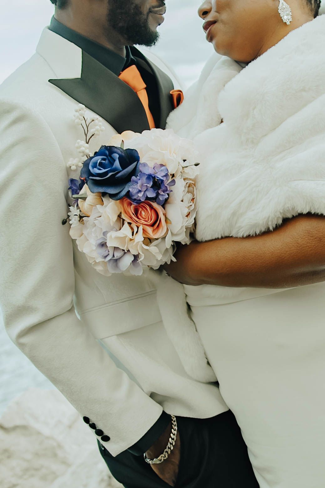 A romantic wedding couple embraces while wearing elegant white and black formal attire with floral accents.