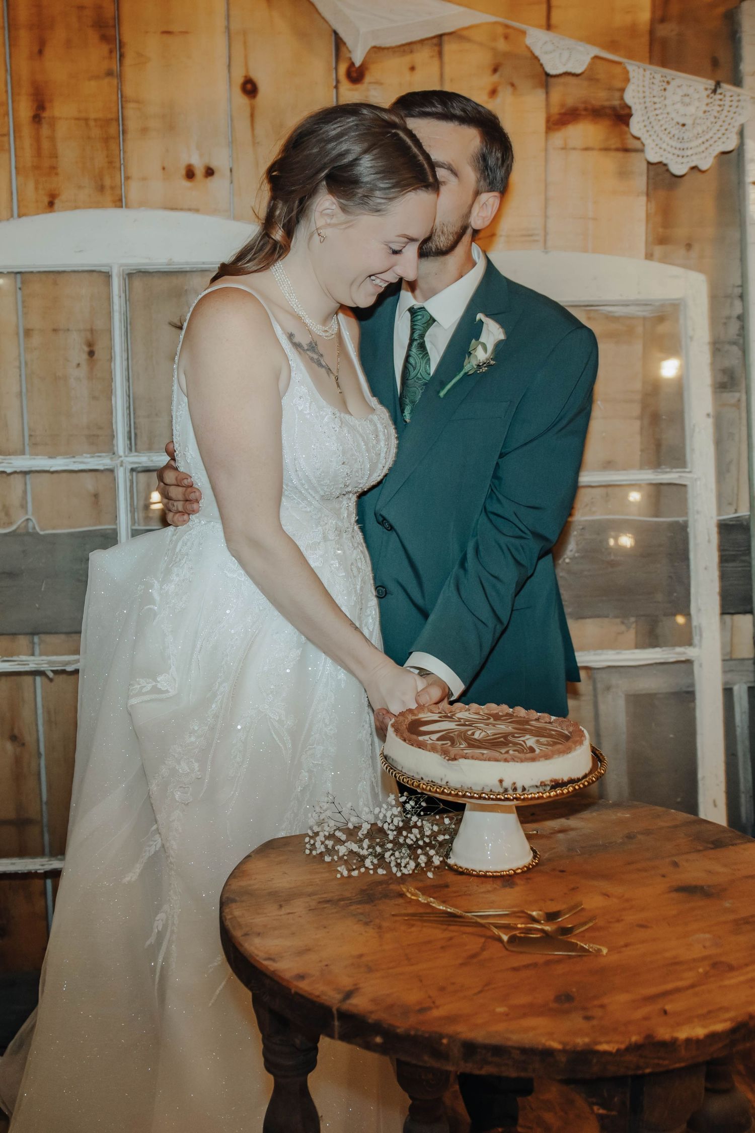 Newlyweds share a sweet moment while cutting their wedding cake in a rustic barn setting.