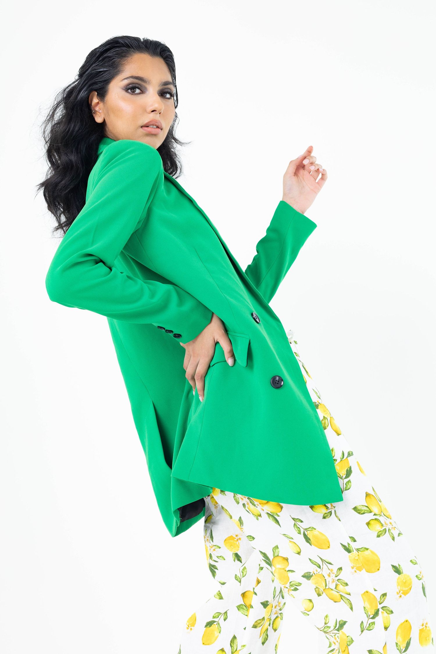 A figure in a vibrant green blazer poses dynamically against white background wearing a yellow floral patterned skirt.