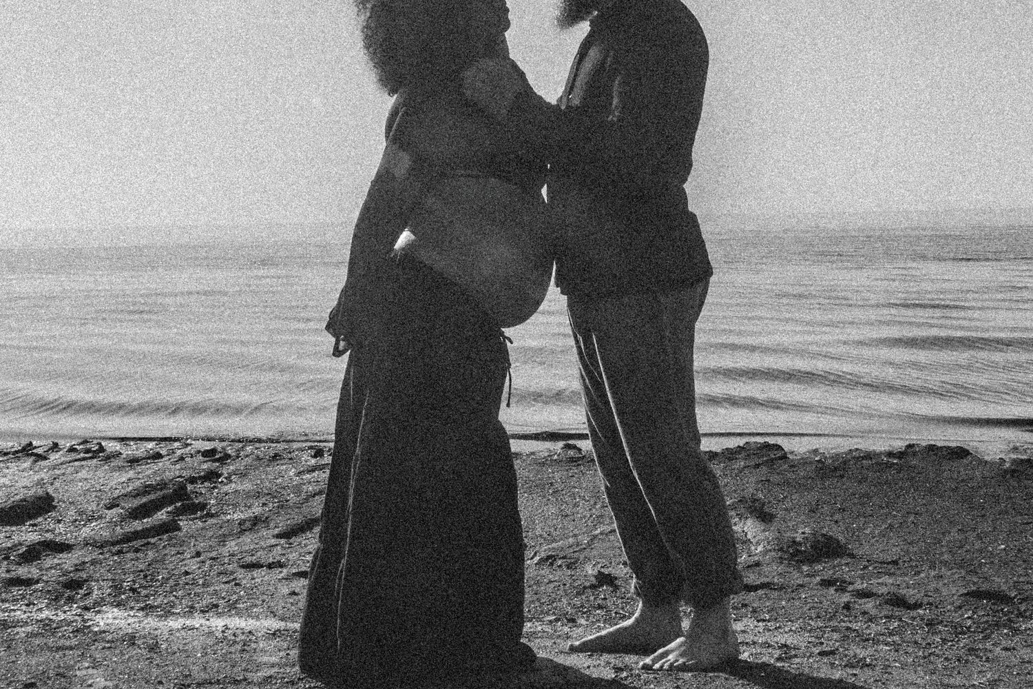 Romantic silhouettes of a couple embracing while standing on a beach in black and white photography.