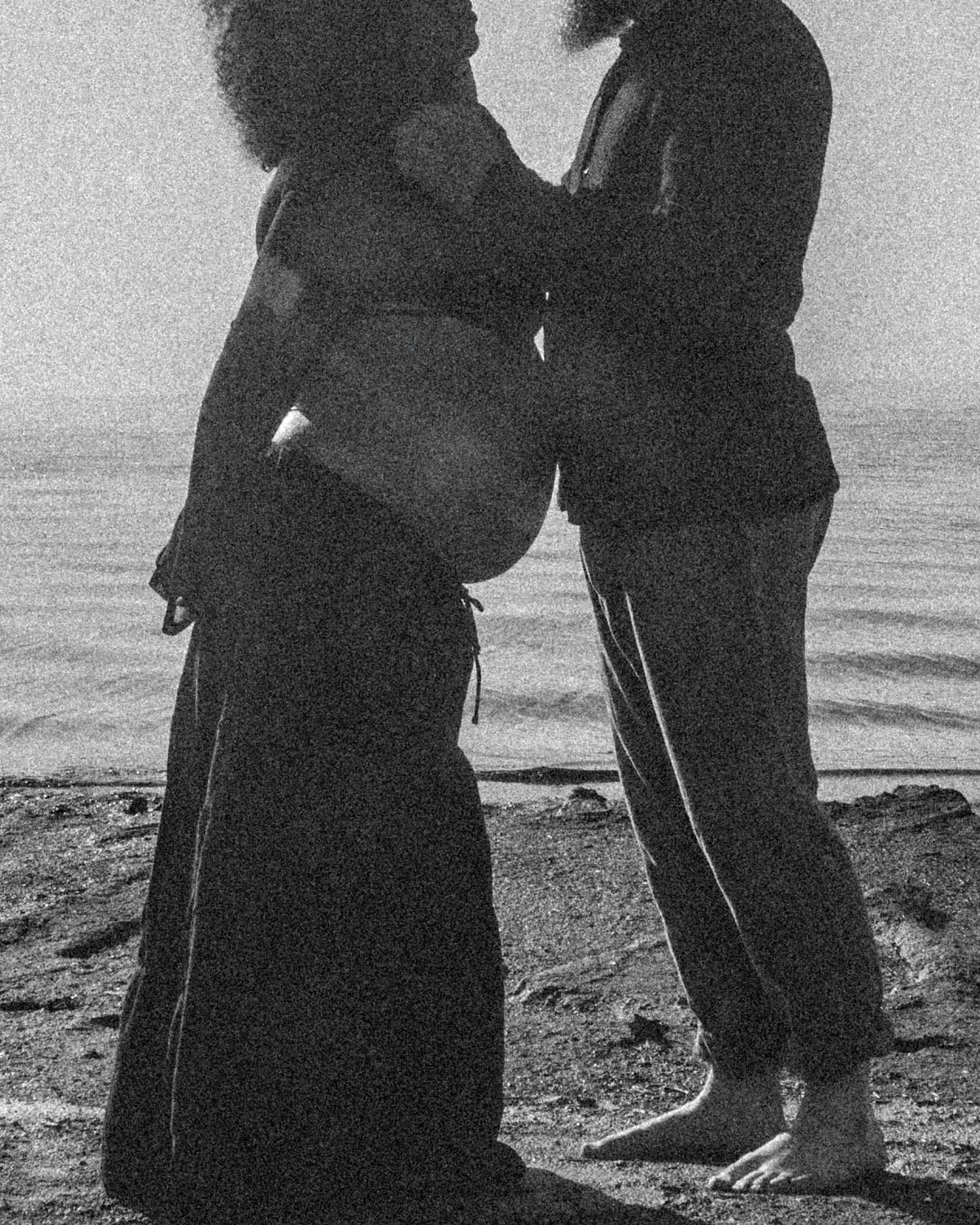 A silhouetted couple walking along a beach shoreline at sunset in a series of connected black and white frames.