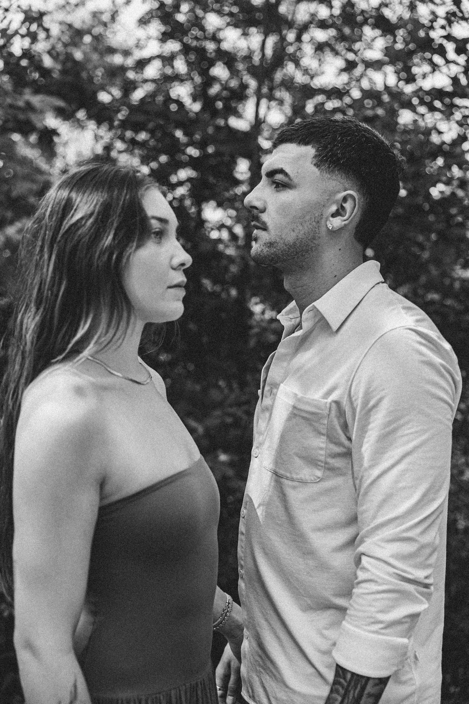 Black and white portrait of a romantic couple standing close together outdoors in a natural setting.