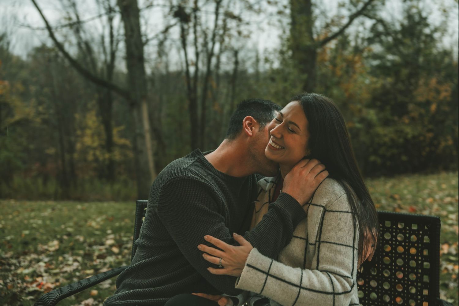 A couple shares an intimate moment in a moody autumn forest setting with dark tones and natural lighting.