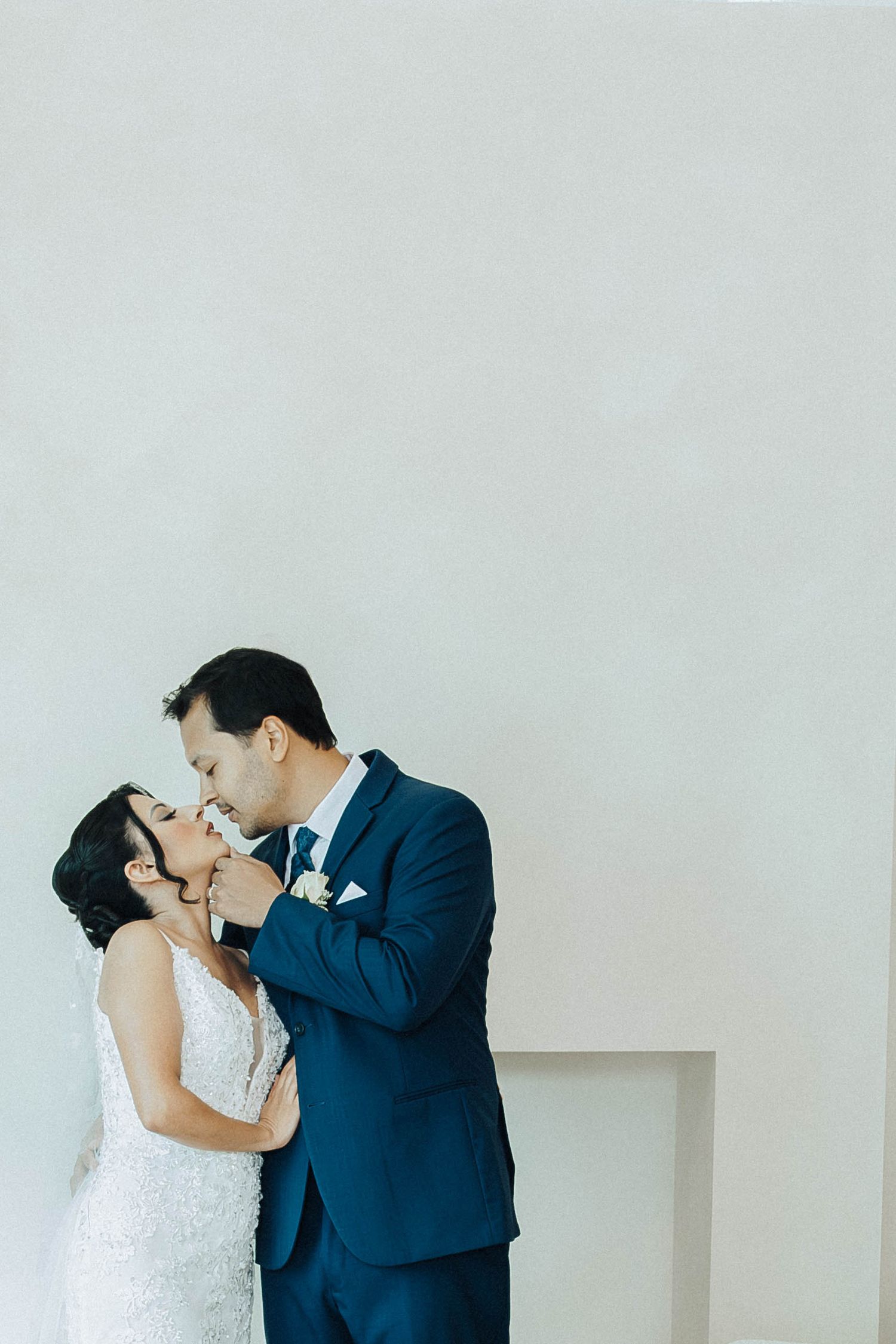 A bride and groom share an intimate kiss in a minimalist white interior during their wedding day.