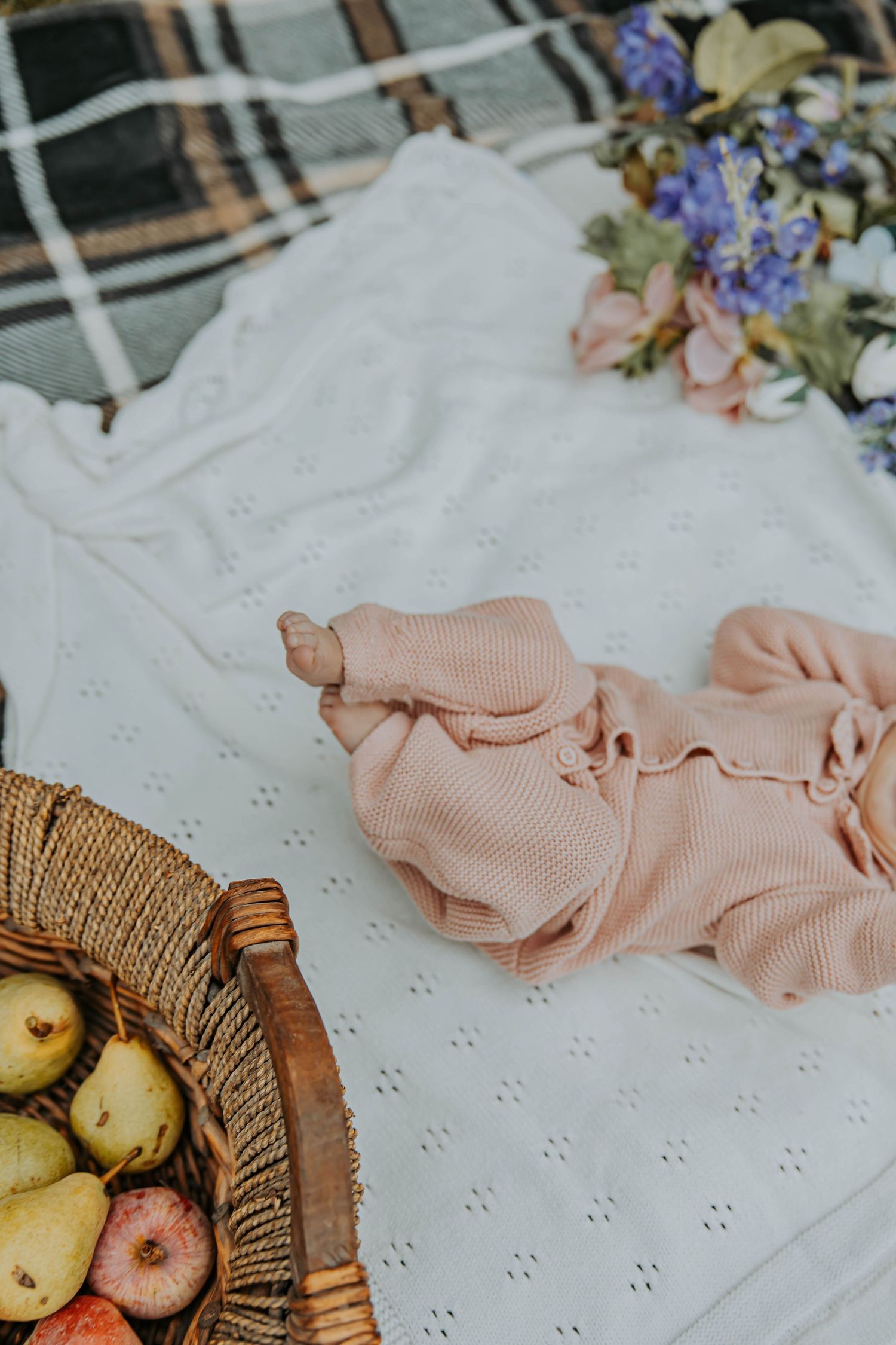 Close-up of textured white fabric with pink ribbons and scattered delicate purple flowers and fruits on the surface.