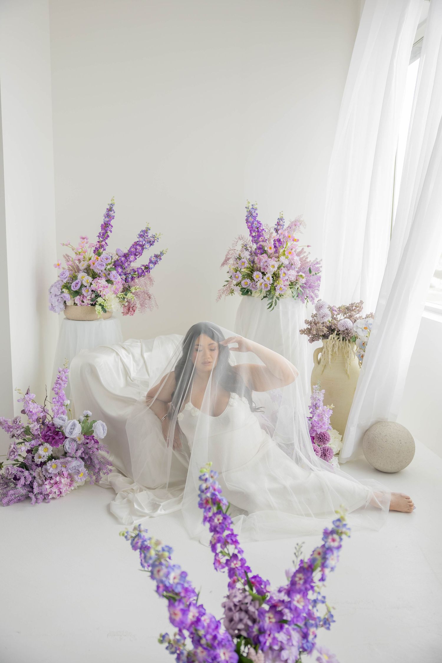 Soft and romantic photography setup with delicate purple flowers and white fabric in natural light.