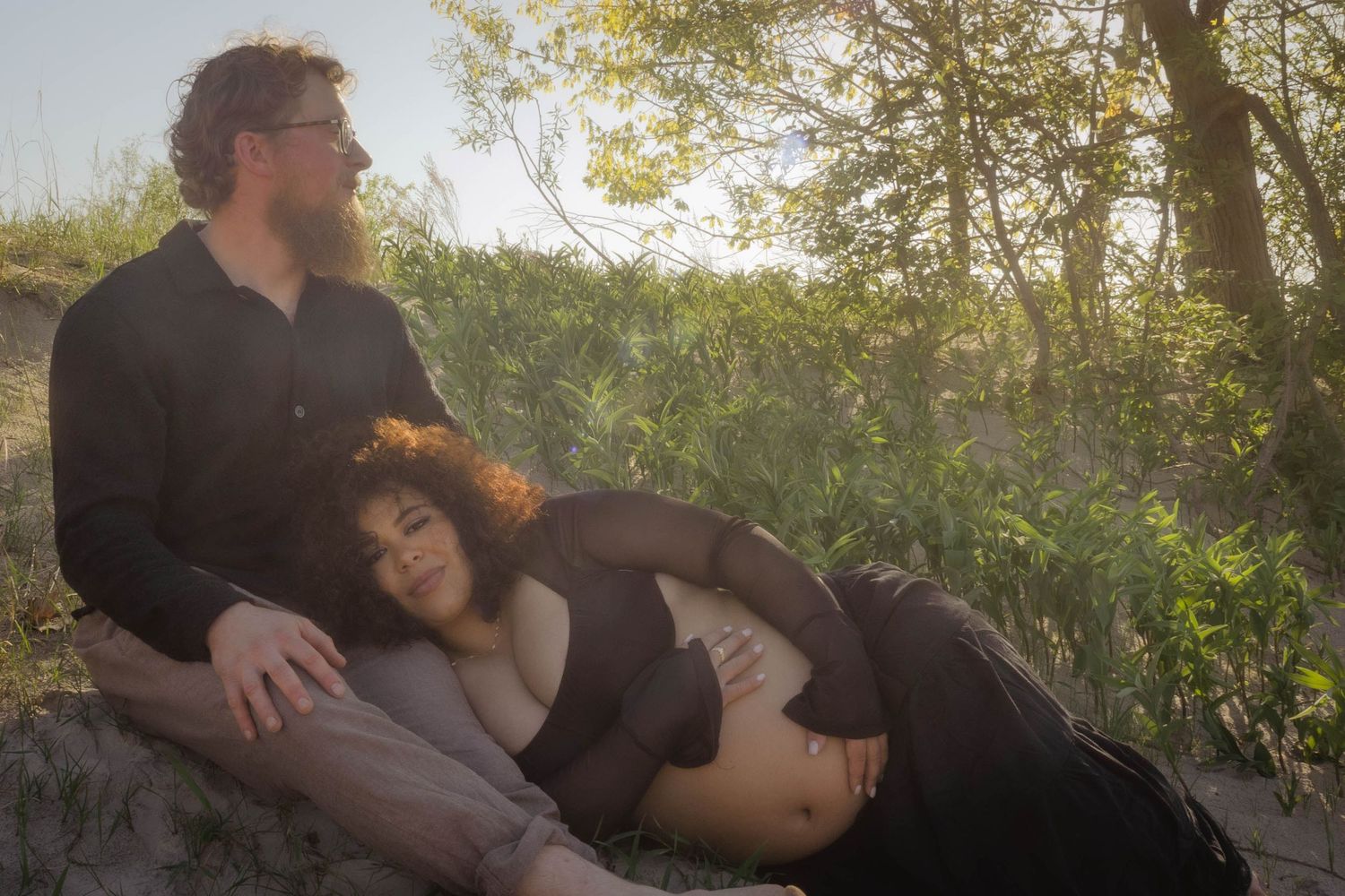 Two people rest together in nature during golden hour with sunlight filtering through trees in the background.