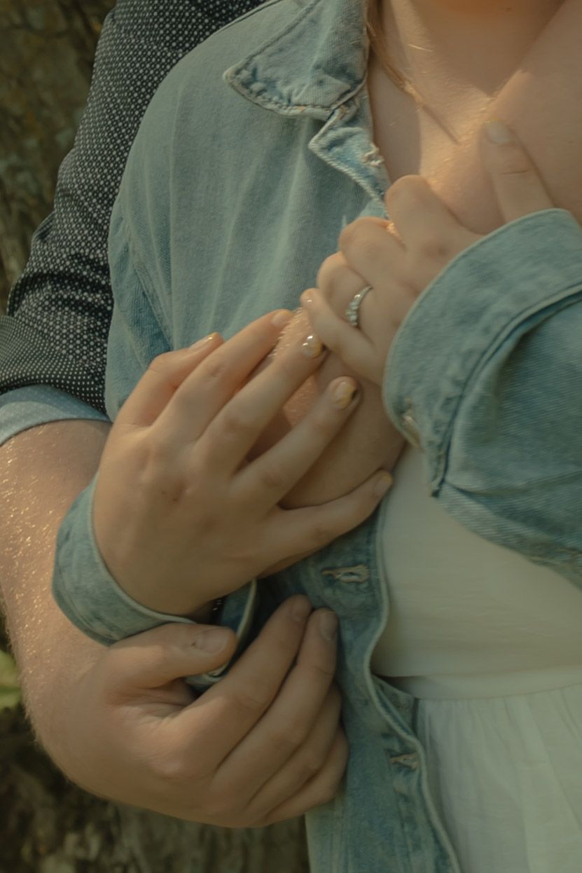 Couple holding hands showing engagement ring in outdoor setting with denim clothing.