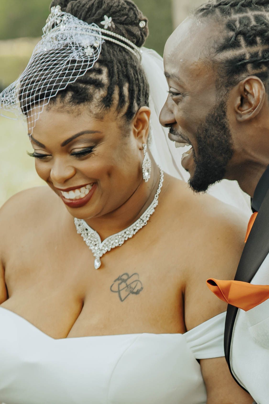 A joyful wedding couple shares an intimate moment in white attire with elegant jewelry details.