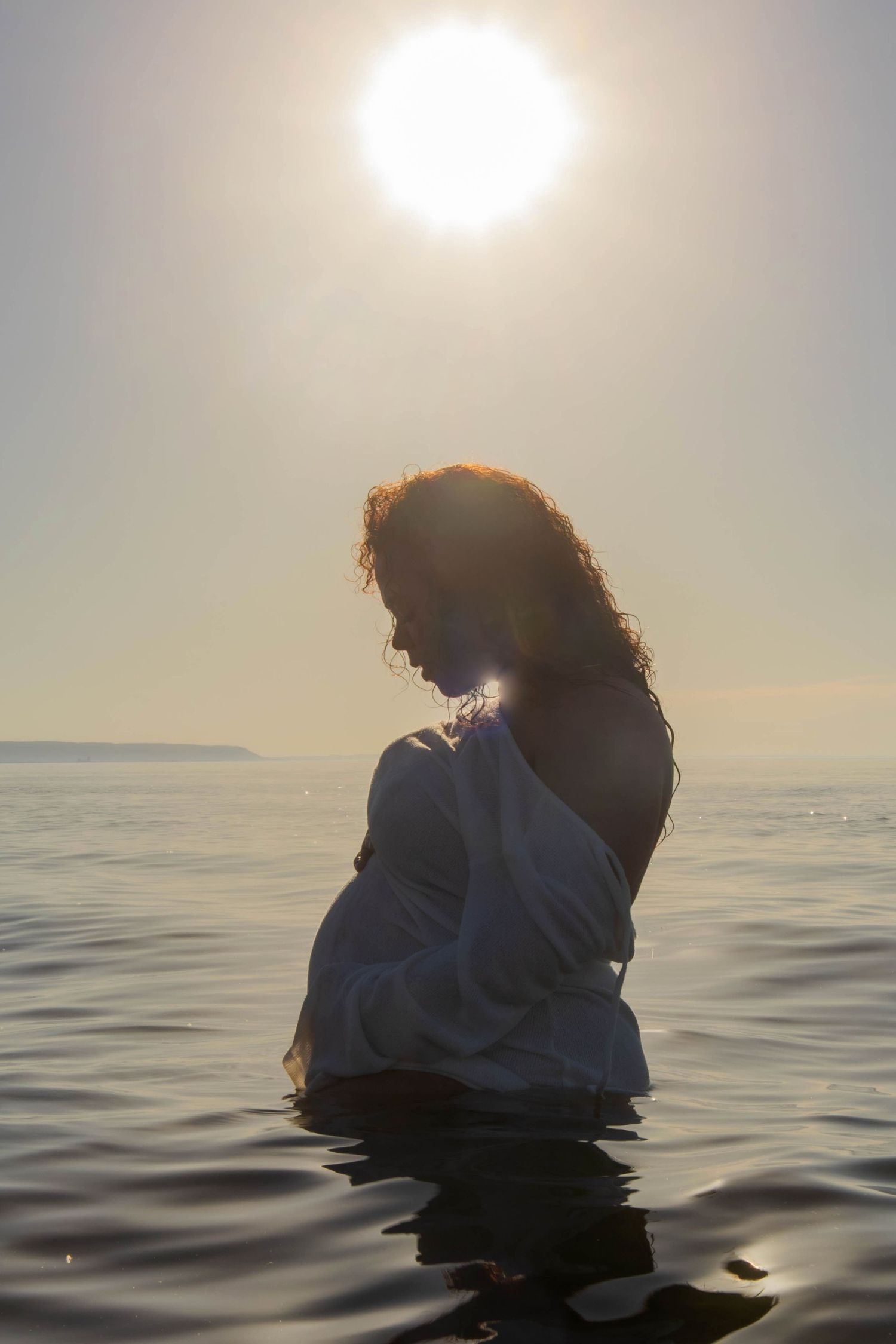 Silhouette in white clothing floating in ocean water against bright sunlight.