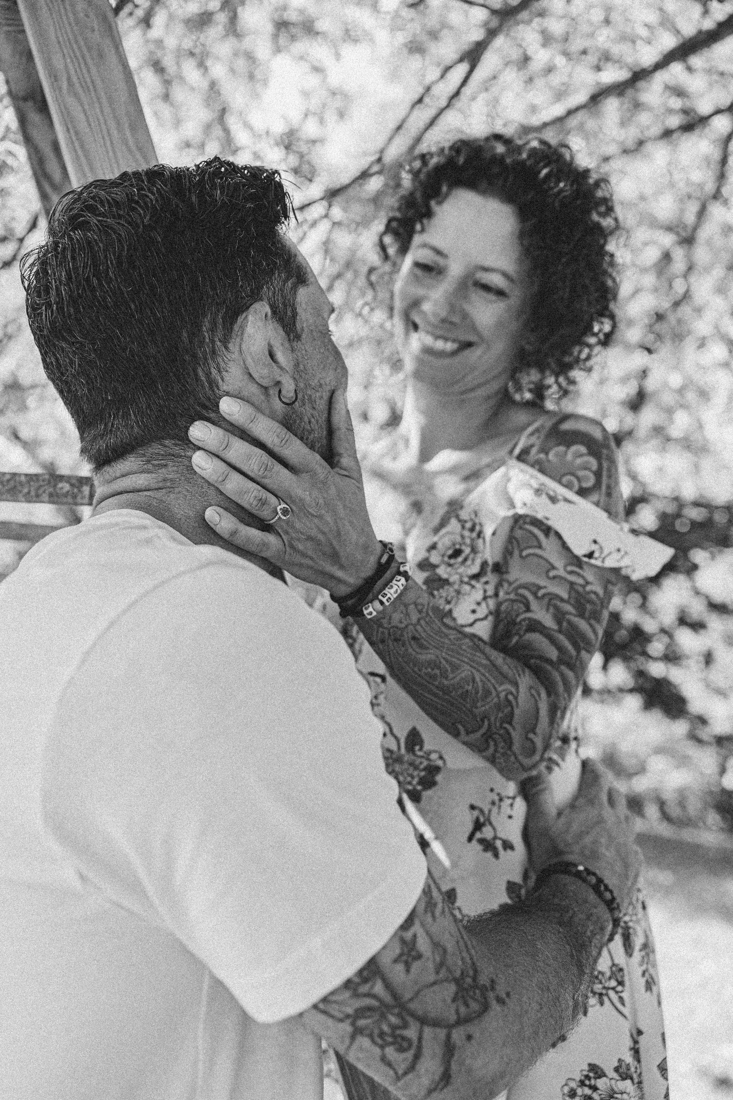 A romantic black and white photo of a couple sharing an intimate moment outdoors under trees.