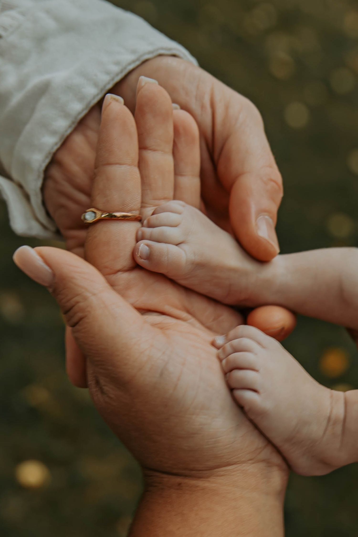 Close-up of hands gently holding a small infant's hand with a delicate gold ring on display in soft natural lighting.