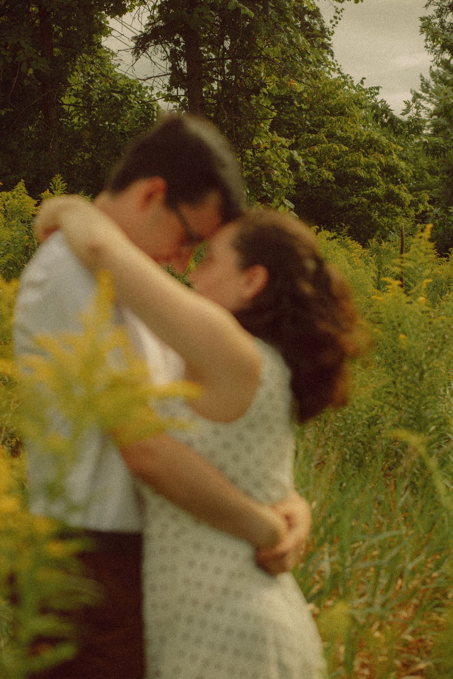 Couple embracing and kissing in a lush green field with yellow wildflowers, romantic outdoor portrait.