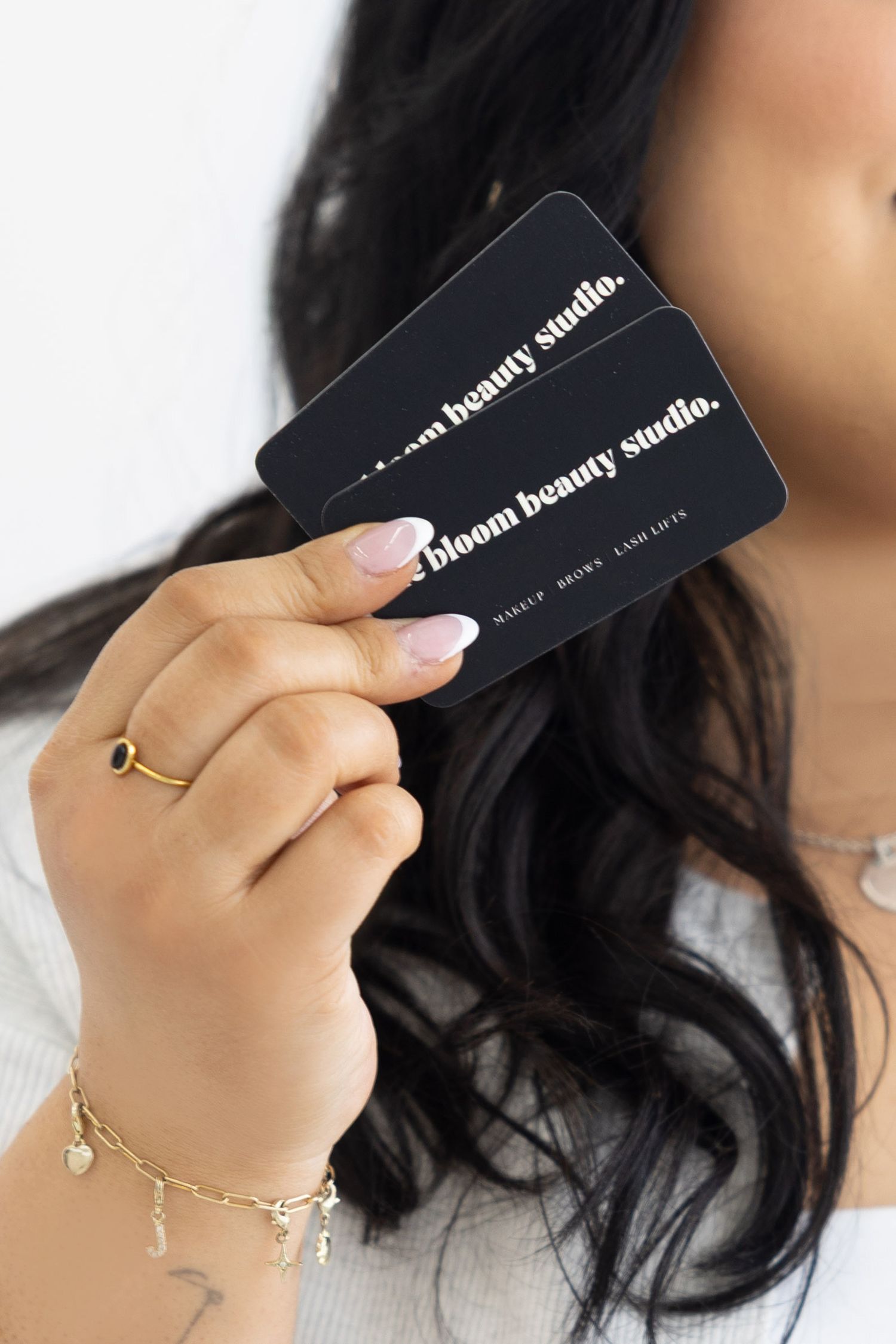Hand holding two black Bloom Beauty Studio gift cards with gold jewelry.
