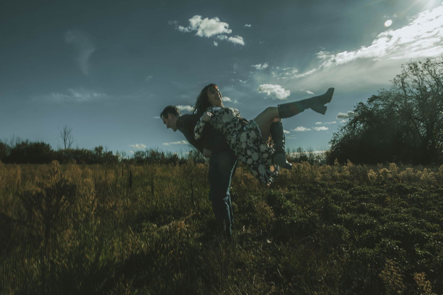 A silhouetted figure performs a dramatic dance pose against a moody sky in a rural field at dusk.