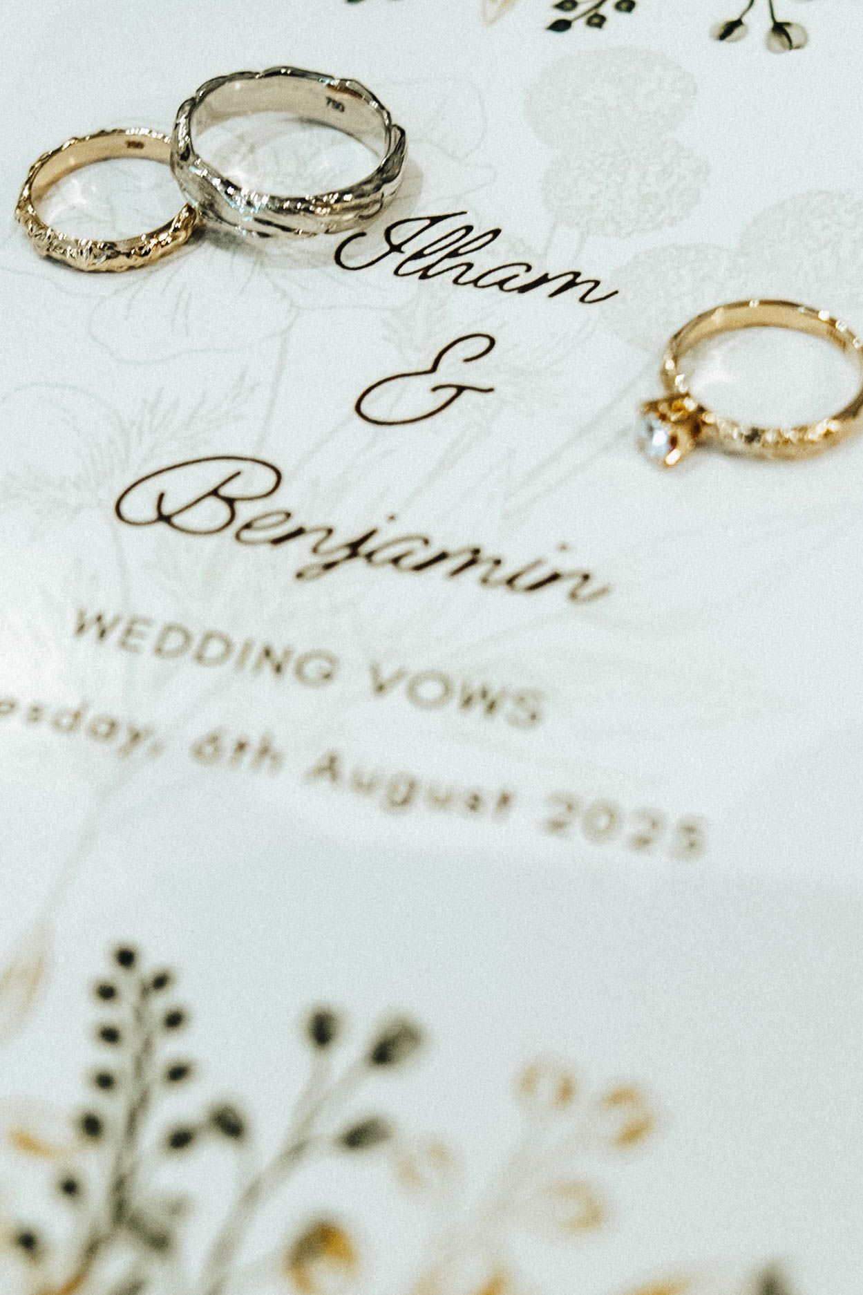 Close-up view of wedding invitation details with elegant calligraphy and gold rings on white paper.