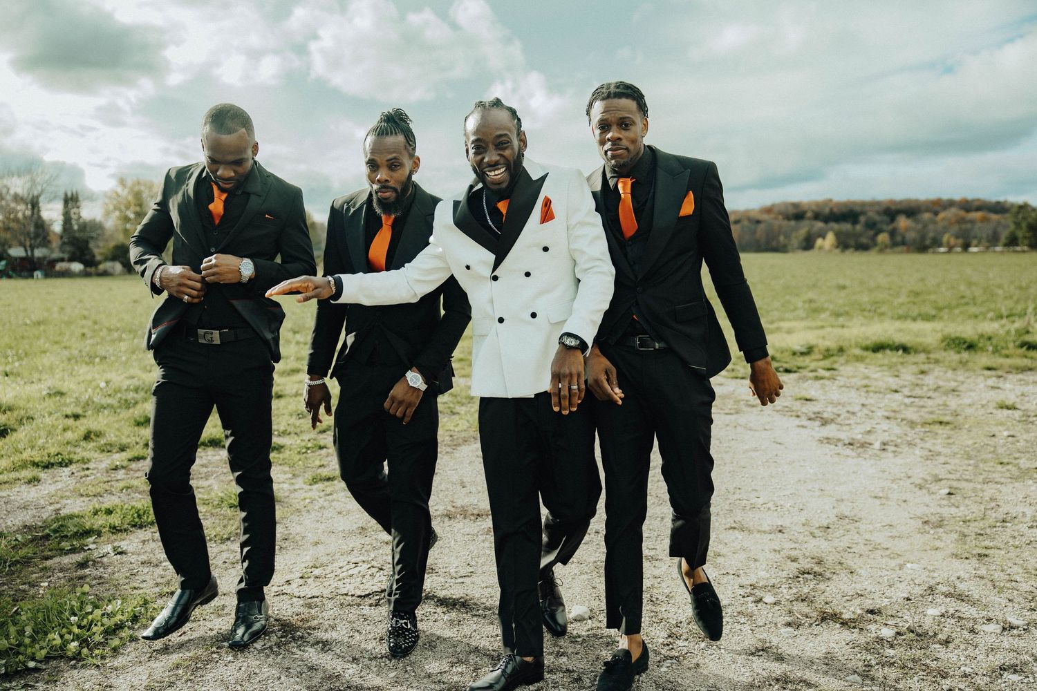 Groomsmen in black suits jumping together for a fun photo in an outdoor field setting.