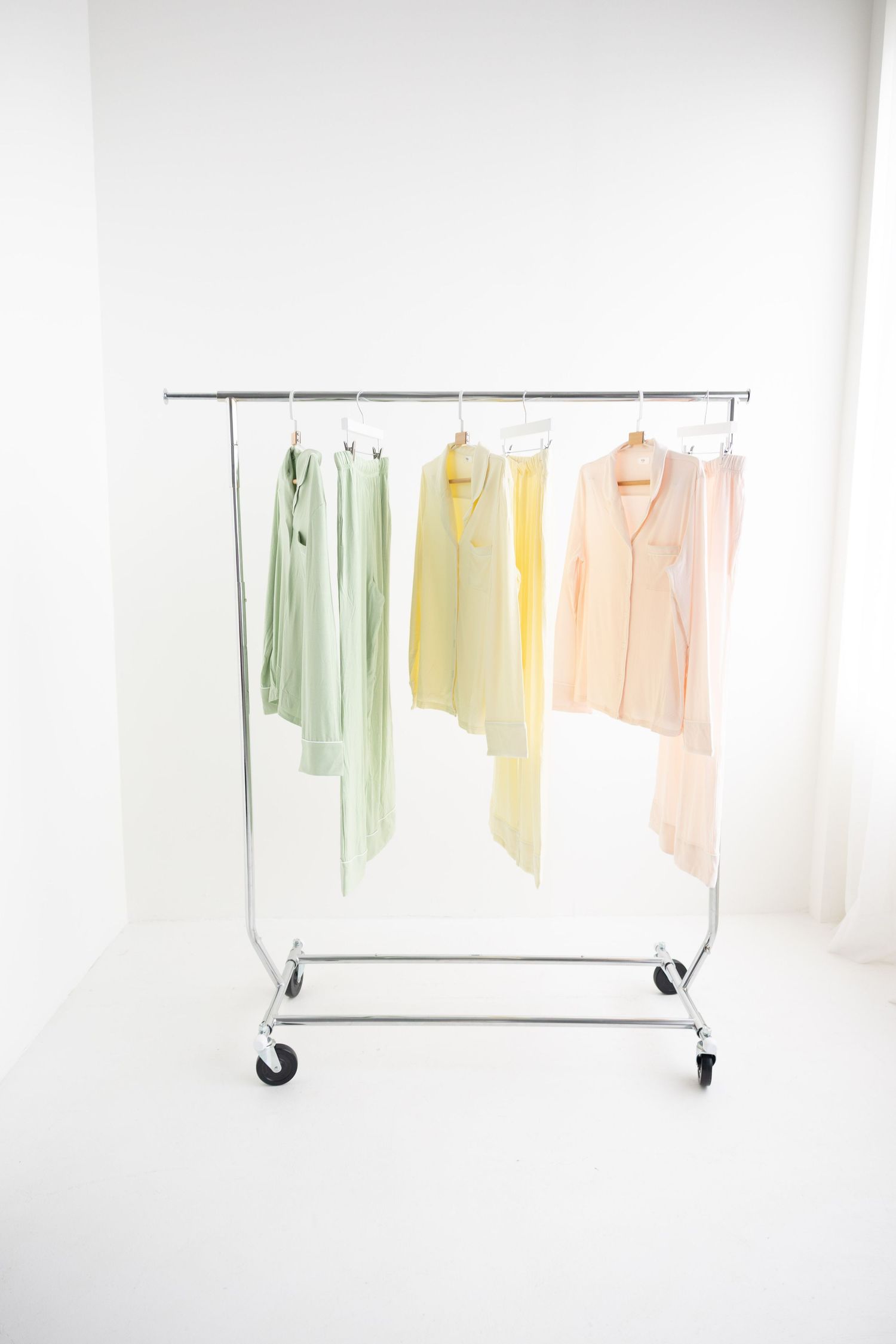 Pastel green, yellow, and pink pajama sets hanging on a rolling clothing rack against a white background.