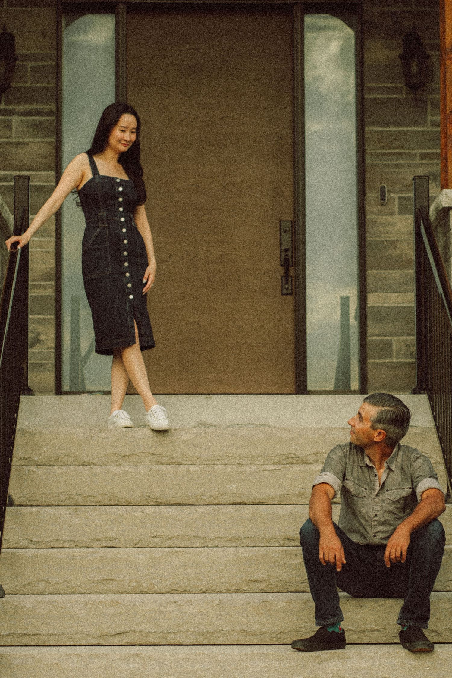 A woman in a black dress walks down stone steps toward a man sitting at the bottom.