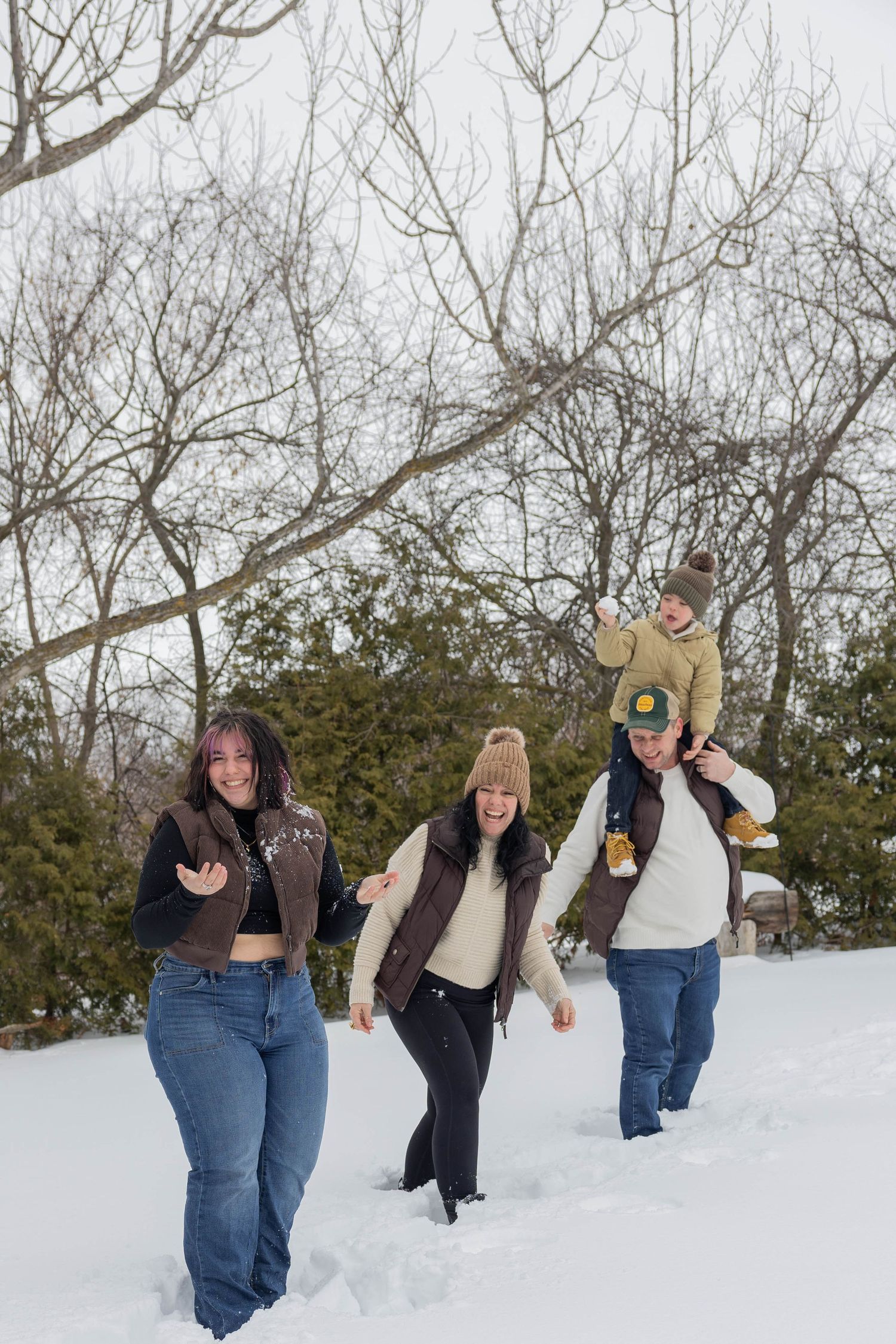 Group of friends playing and posing together in deep winter snow with bare trees in background.