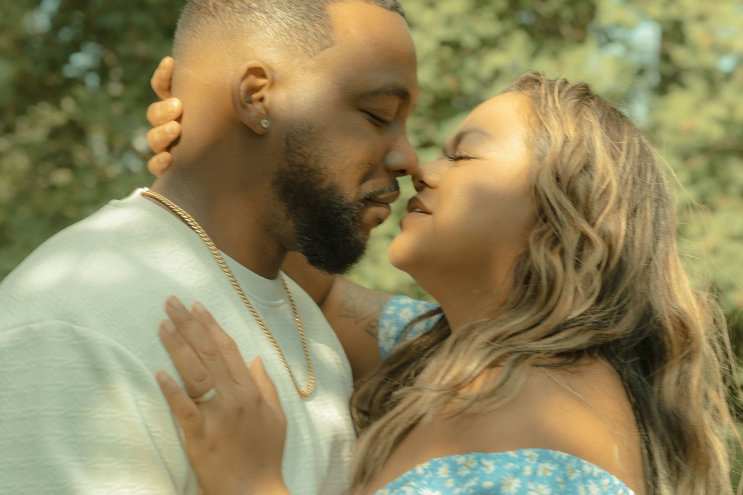 Couple sharing a romantic almost-kiss outdoors, woman wearing engagement ring in soft natural light.