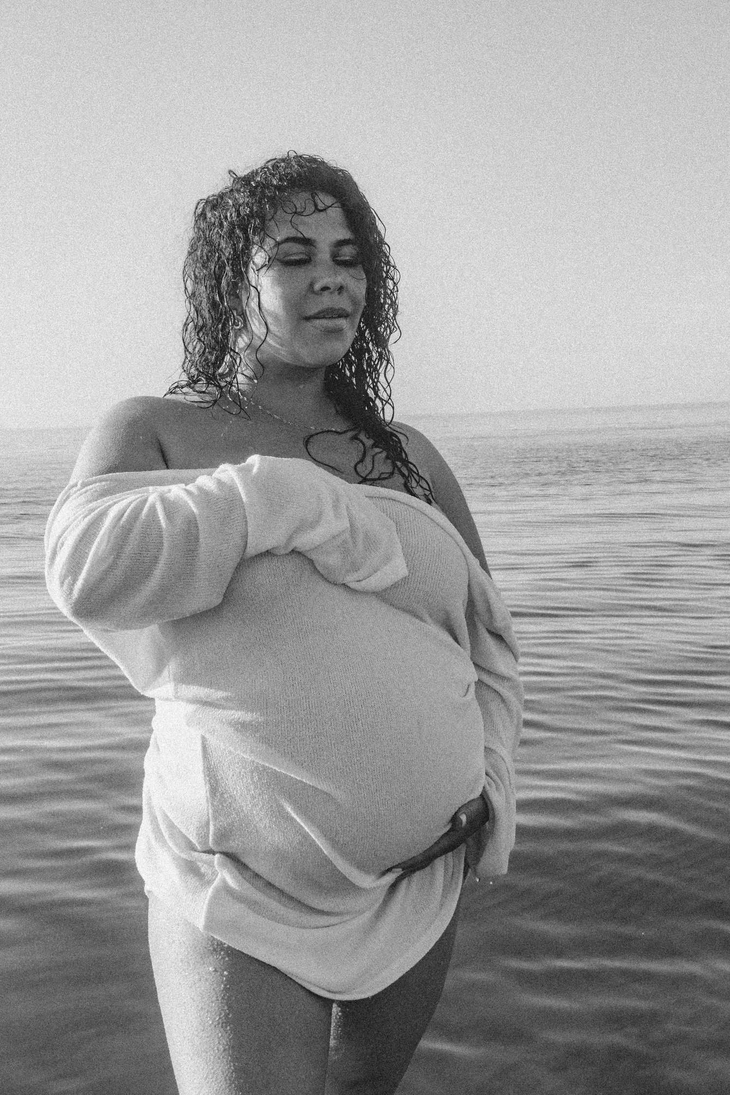 Monochrome image of person wearing white sweater standing in calm ocean waters.