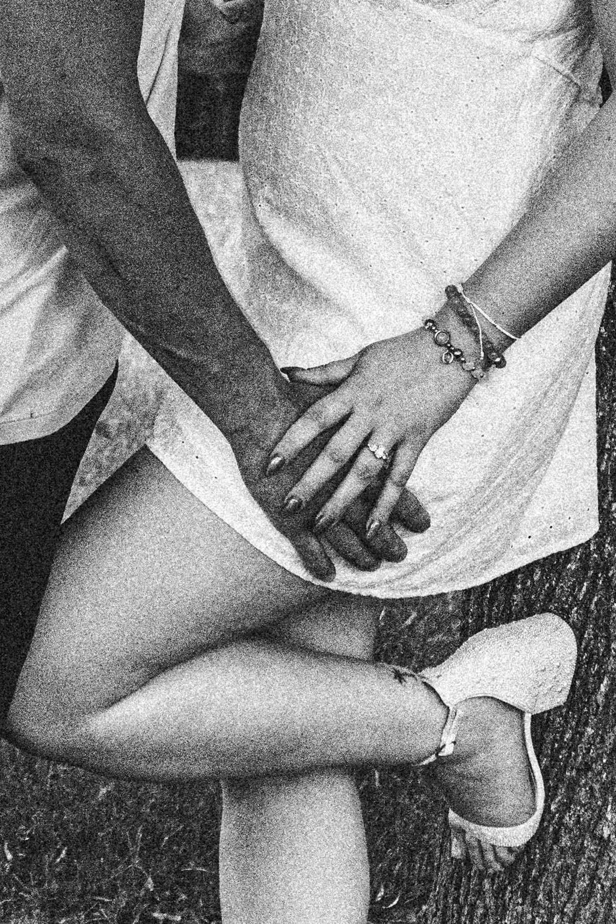 A black and white close-up photo shows hands clasped in a lap while wearing a light-colored dress and white shoes.