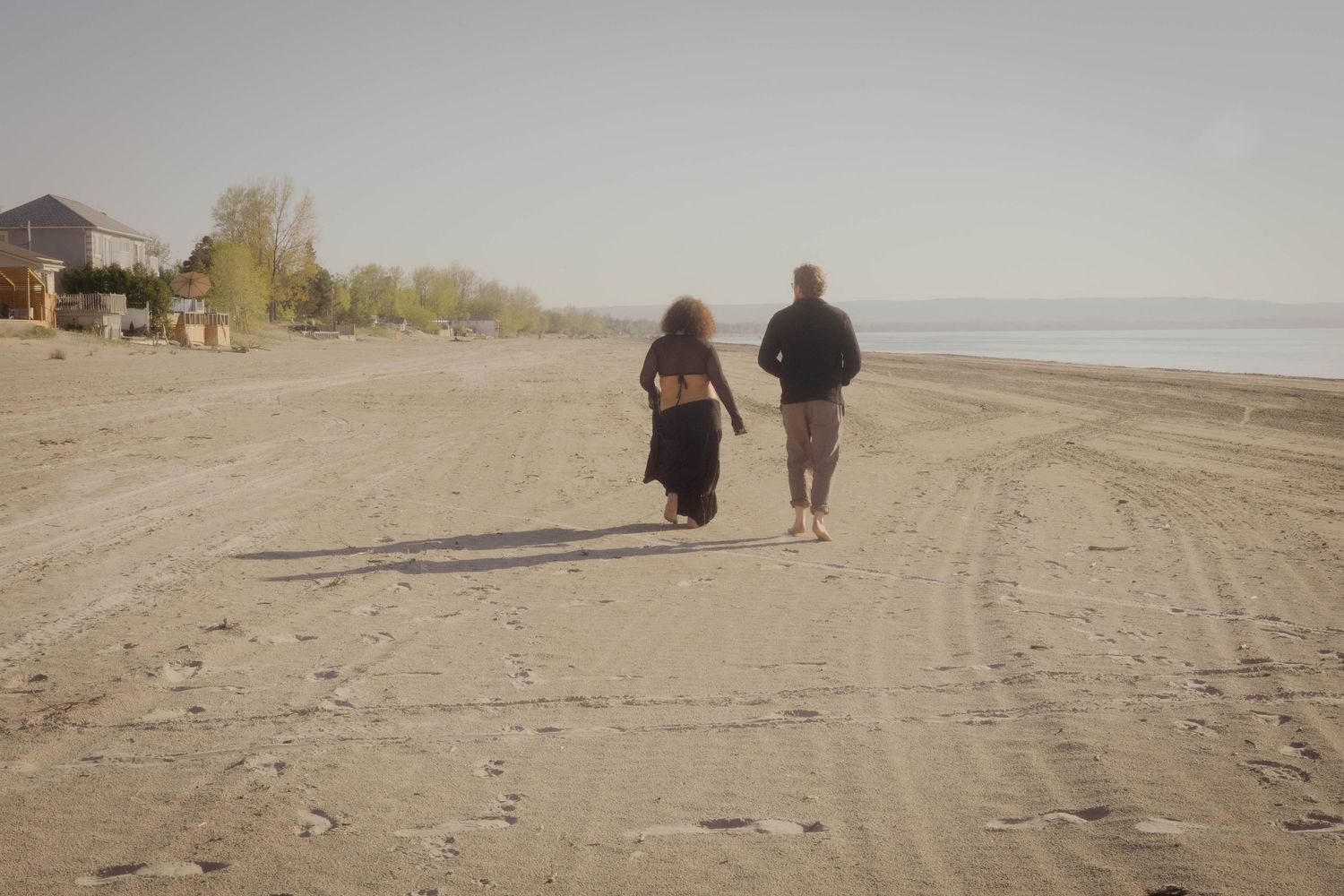 People walking together on a sandy beach at sunset cast long shadows along the shoreline.