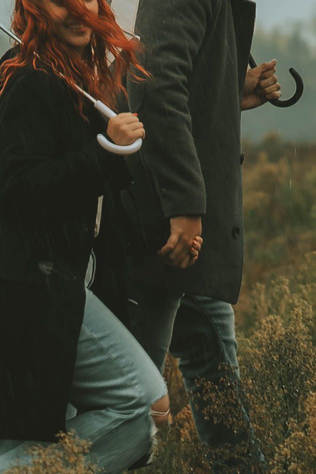 Person wearing black jacket and gray pants poses in a field during golden hour.